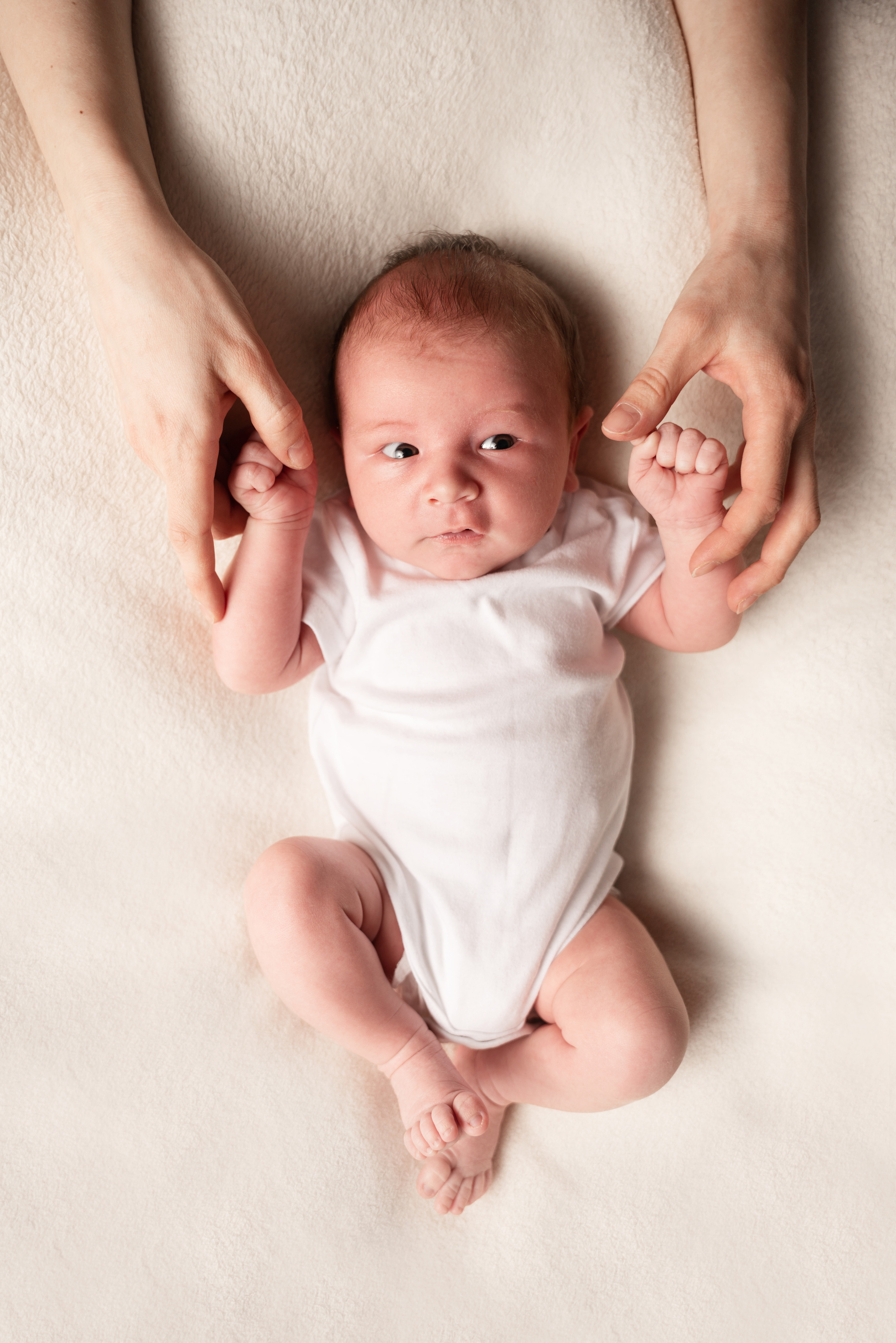 das Baby liegt auf dem Rücken und hält seine Hände an den Händen seiner Mutter fest
