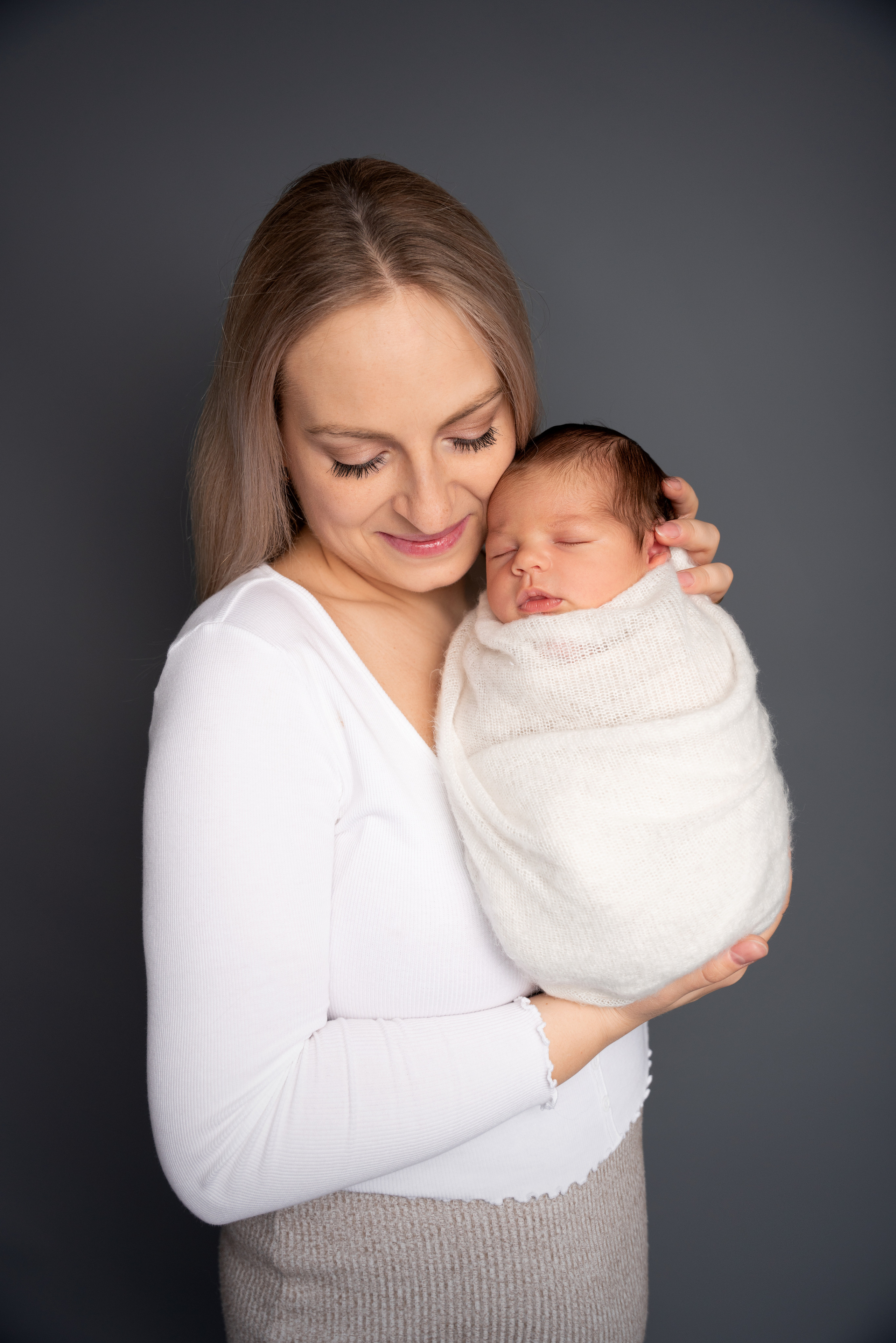 mutter und neugeborener Sohn in weiß auf grauem Hintergrund