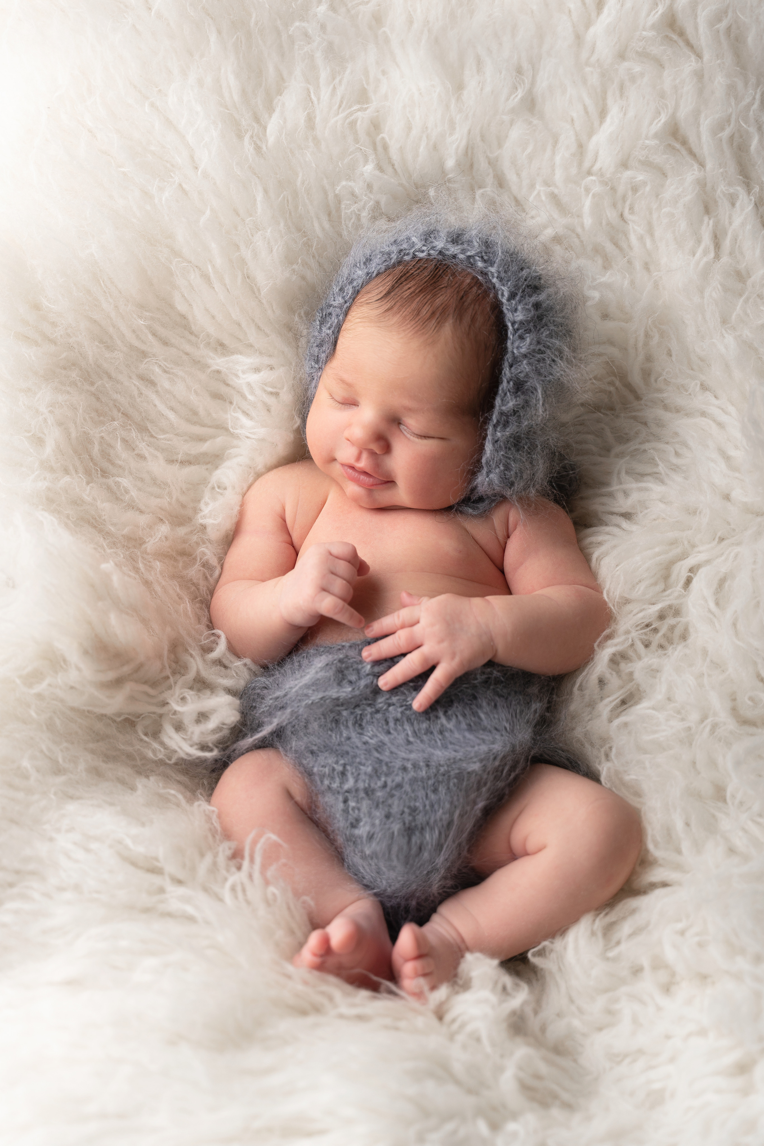 neugeborenes Baby in einem grauen Anzug auf einem weißen Flokati