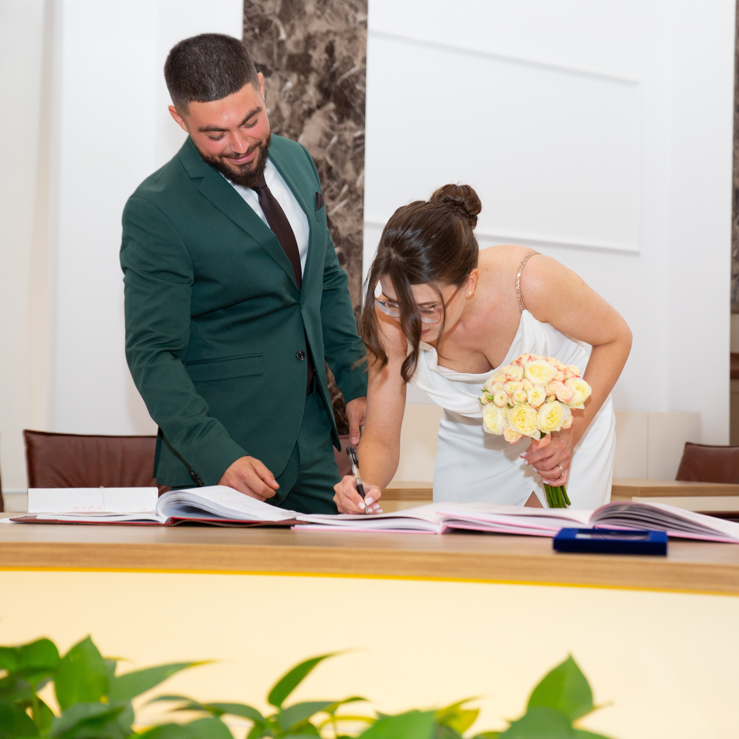 Bride in white dress with bouquet signing a register during a civil wedding ceremony.