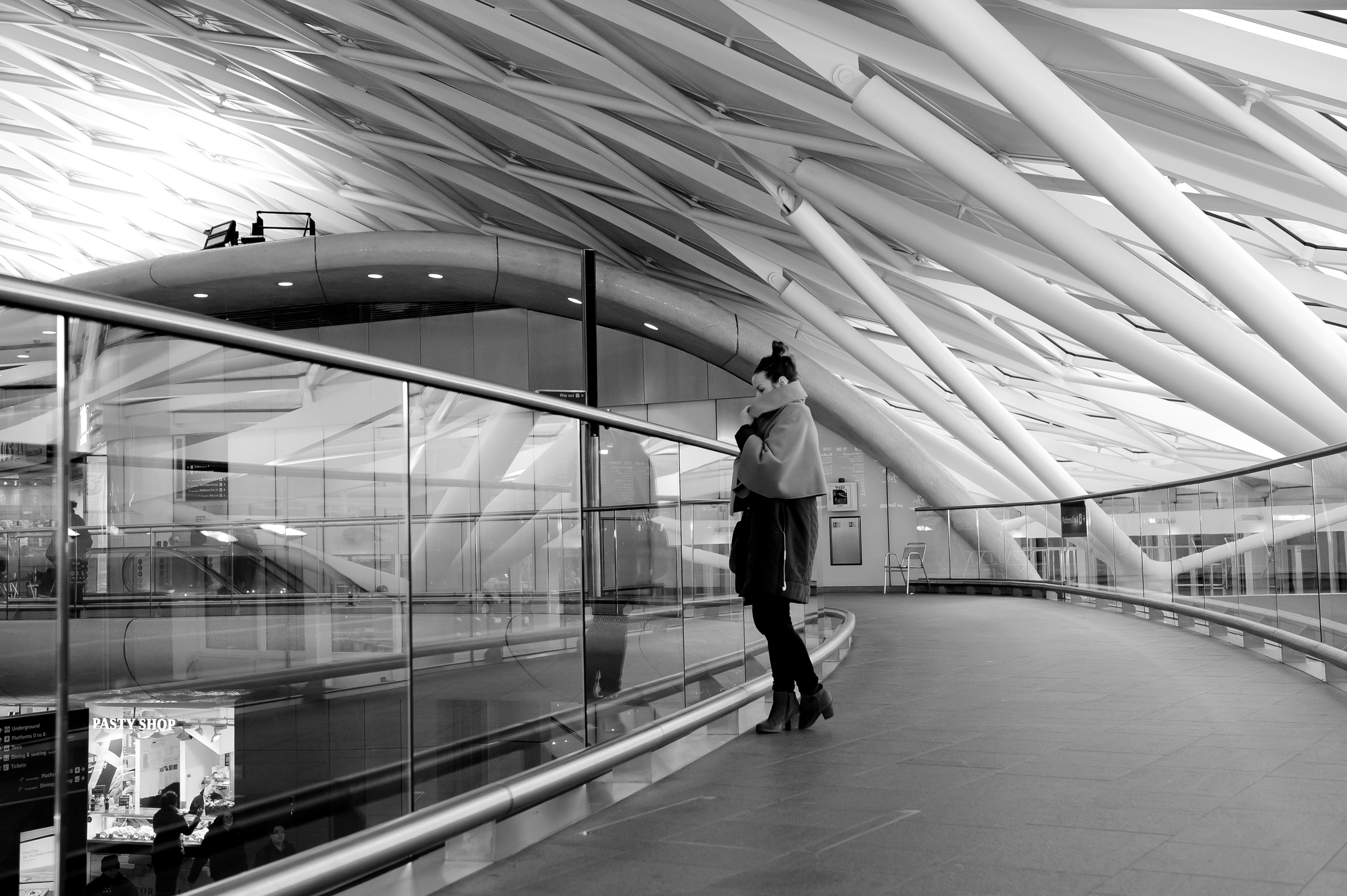 A woman stands on a glass bridge in the concourse of King's Cross station.