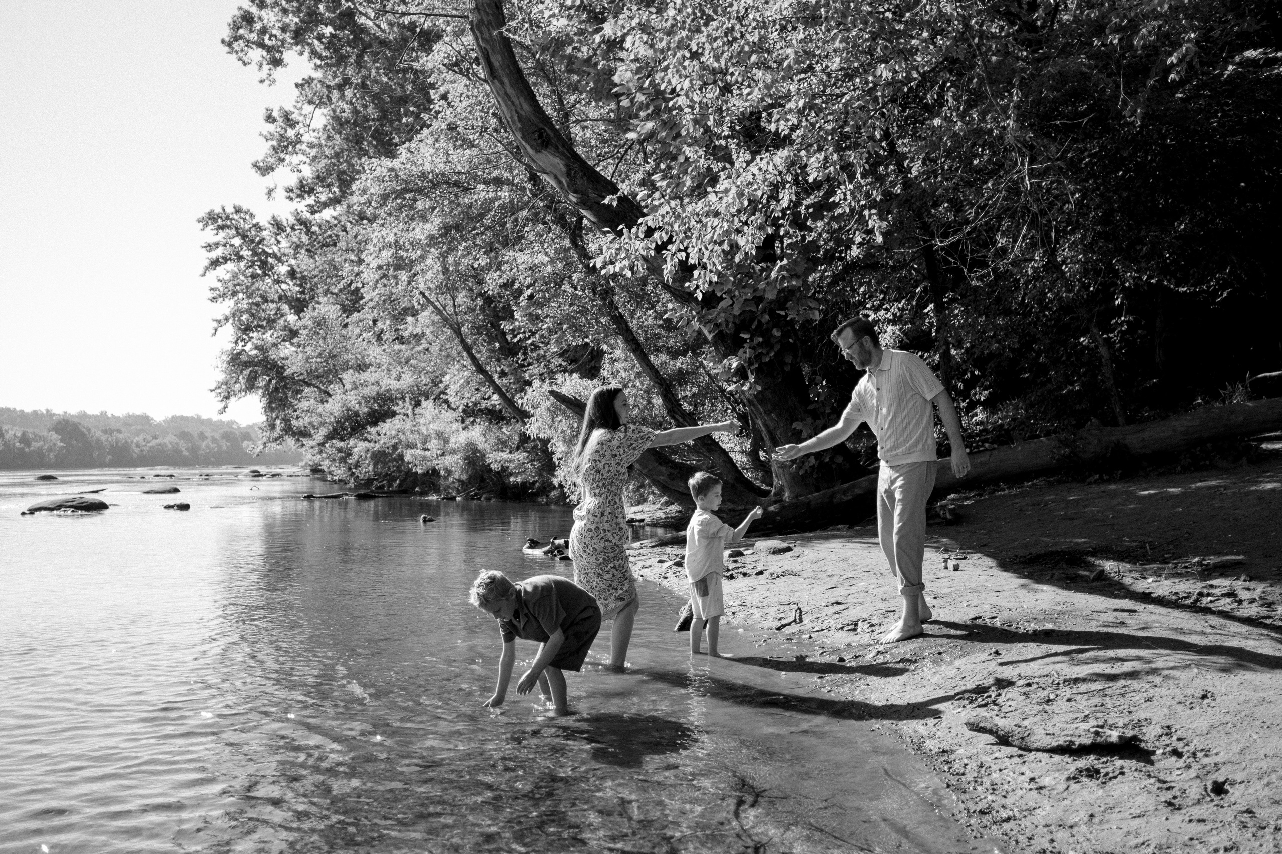 A wide documentary photo showing a family exploring the natural shoreline and green river grass at Pony Pasture