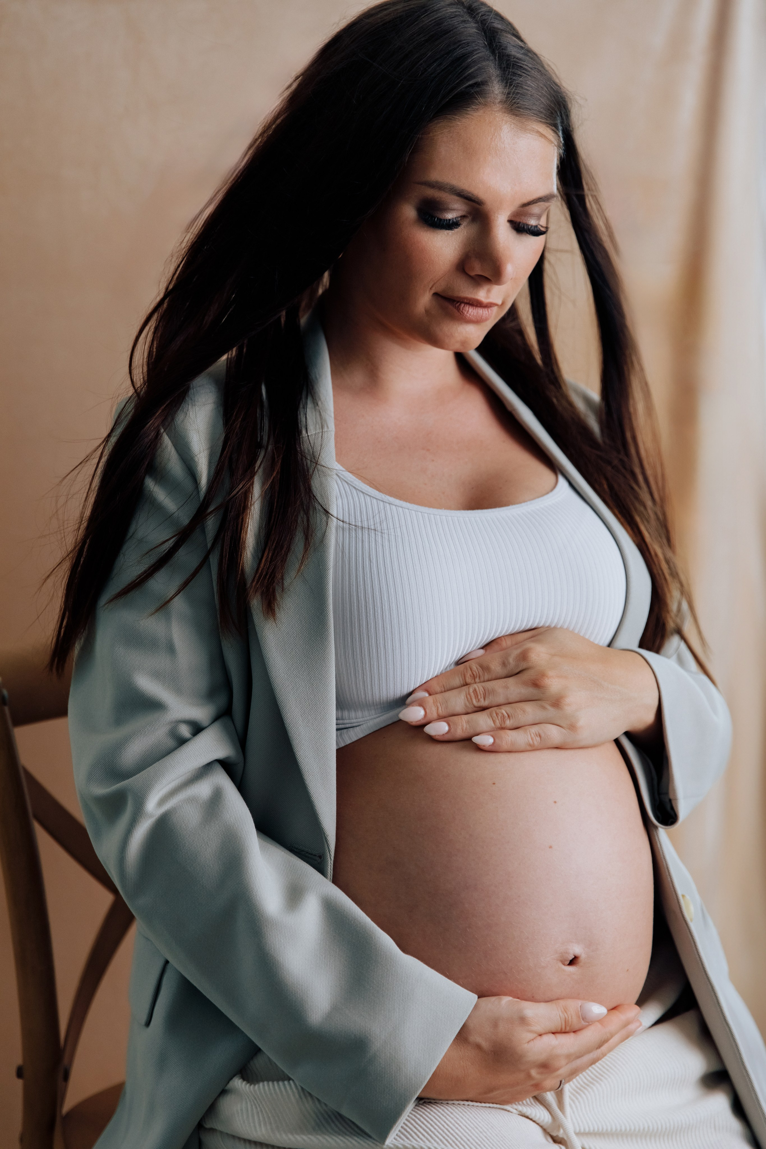 Stilvolle schwangere Frau schaut liebevoll auf ihren Babybauch während eines Fotoshootings