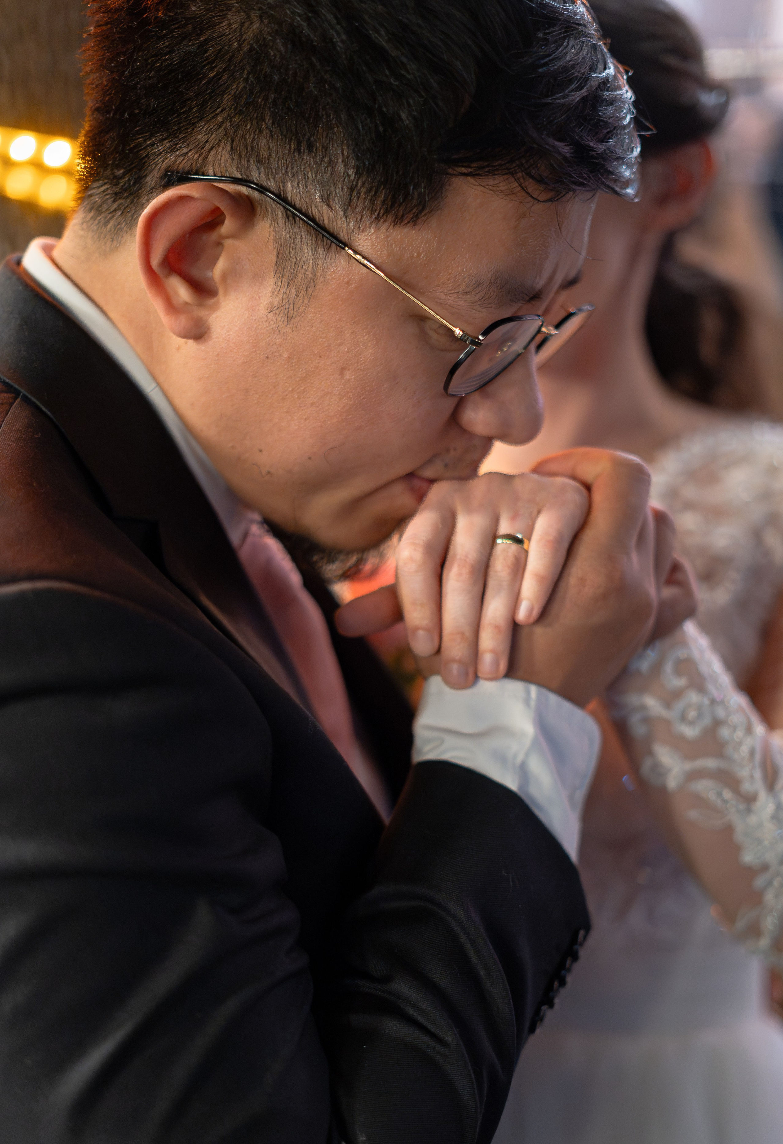 Mire sărutând mâna miresei, detaliu verighetă de aur, lumină caldă de interior, fotografie de nuntă emoționantă, incadru.ro.