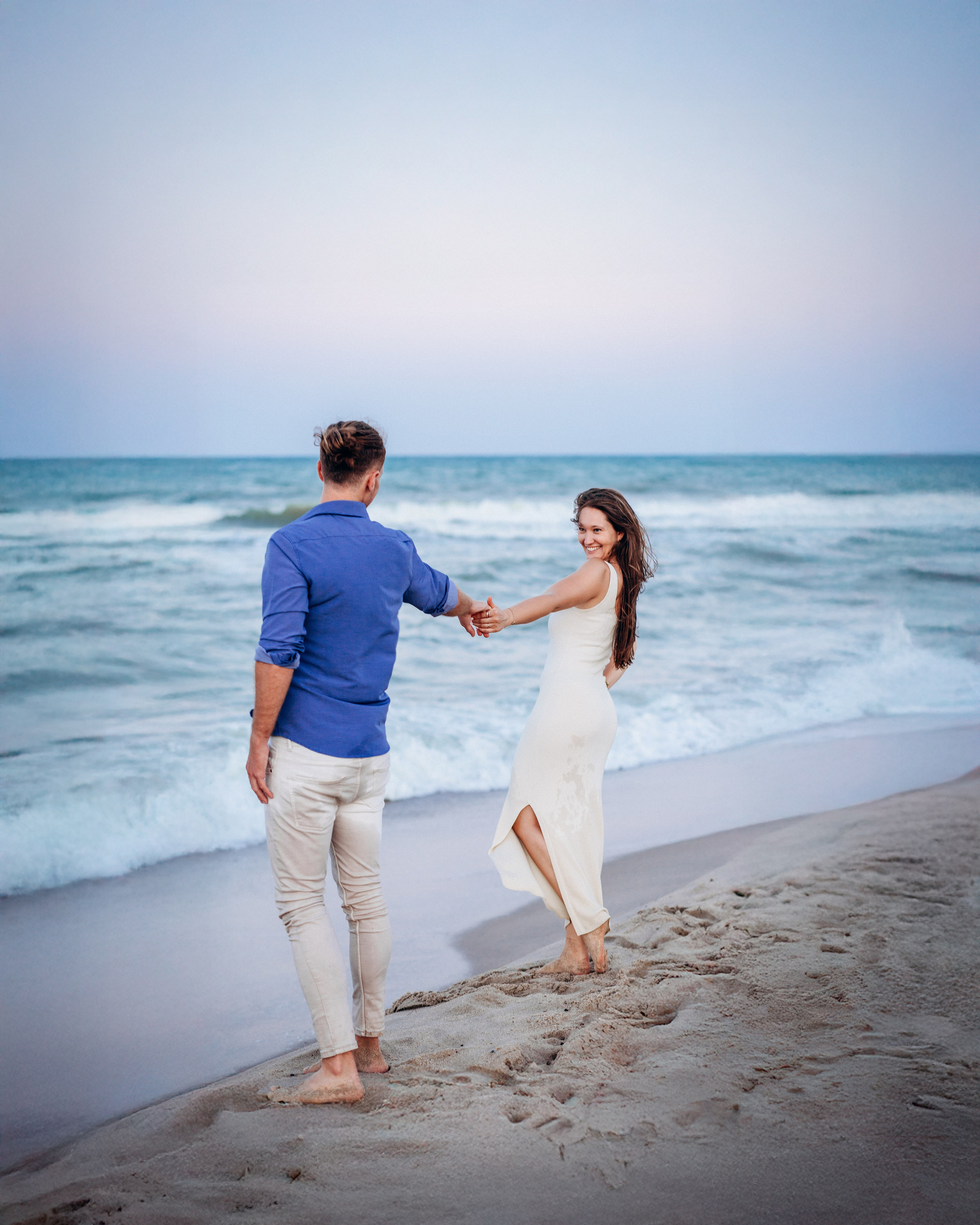 Pareja alegre tomados de la mano durante una sesión de fotos en la playa de Valencia, España — un momento divertido y romántico capturado para sesiones de fotos de pareja o love story en Valencia y en destinos costeros de toda España.