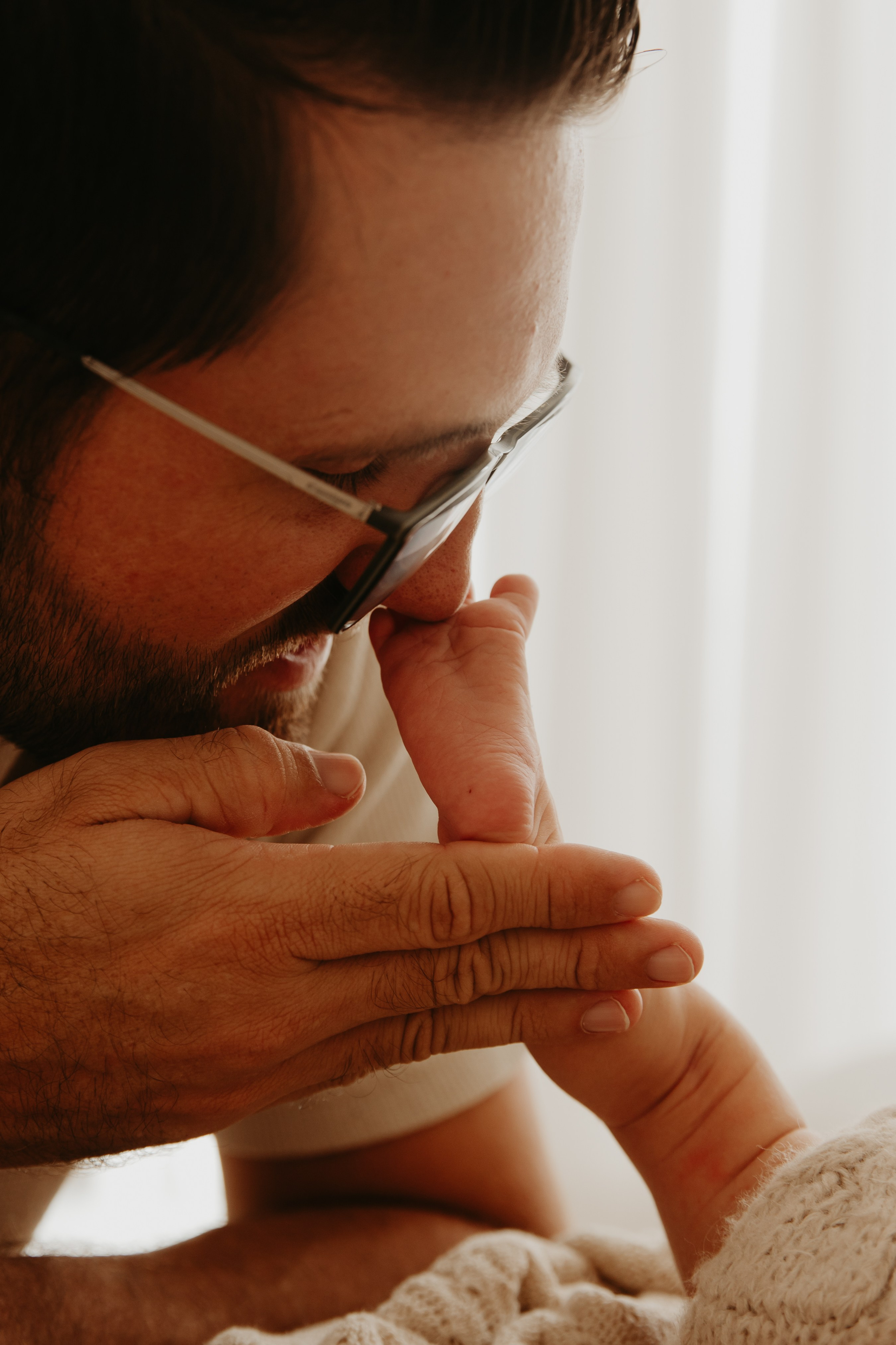 pai faz carinho nos pés de bebê em ensaio newborn com luz natural em Sorocaba