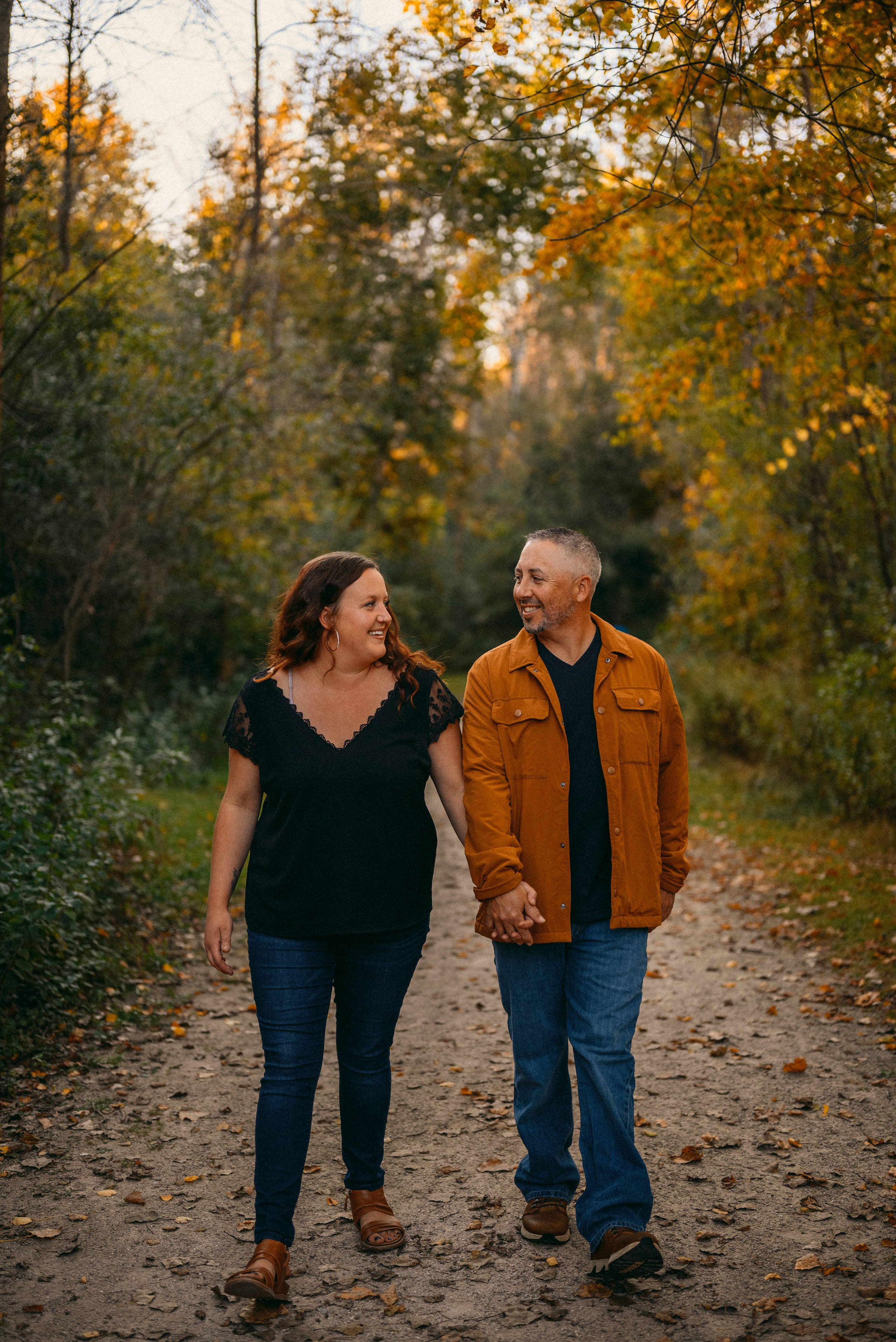 Romantic engagement photo session in De Pere, Wisconsin - couple walking hand-in-hand through a sun-dappled natural setting during golden hour.