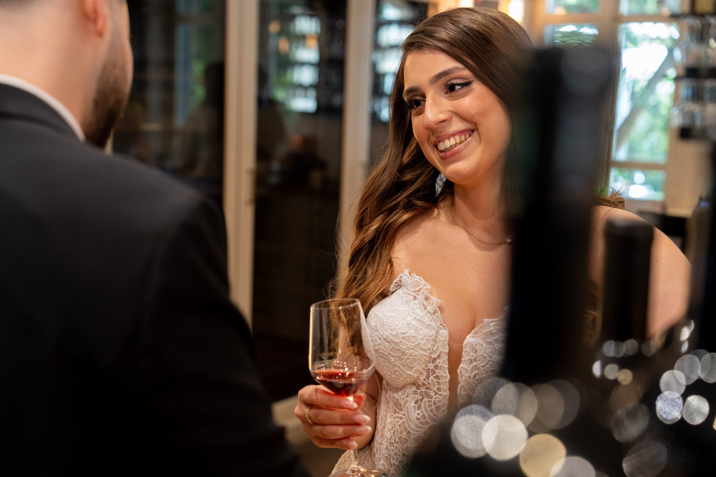 A bride holding a wine glass shares a warm look with the groom