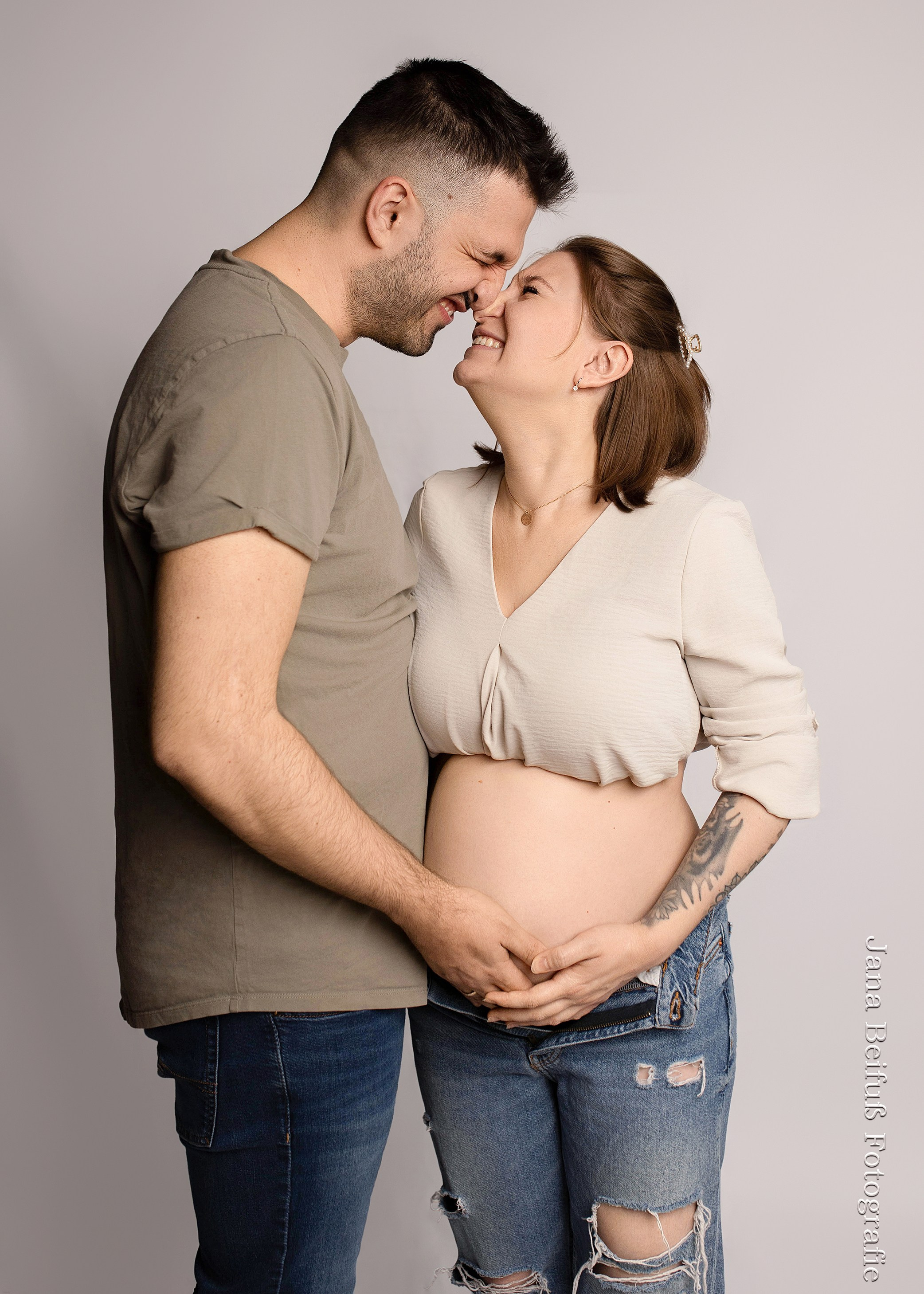 werdende glückliche Eltern in Jeans und geben sich Eskimokuss Nase an Nase in hellen Oberteilen - beim Babybauchshooting bei Jana Beifuß in Weißenhorn bei Erbach - Schwangerschaftsfotografie Weißenhorn bei Ulm