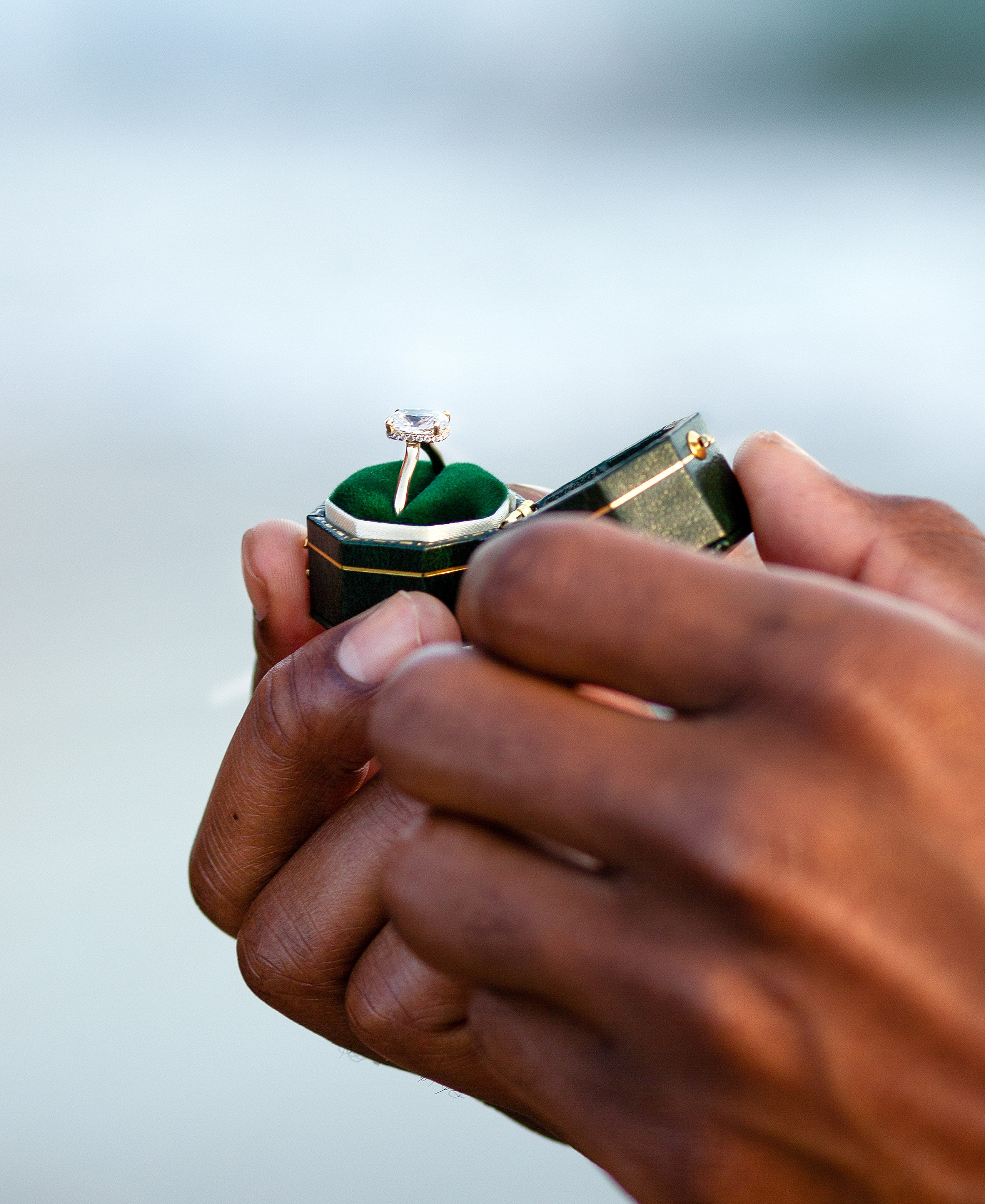 Primer plano de una mano sosteniendo una caja de terciopelo verde con un anillo de compromiso durante una propuesta romántica en la playa en Valencia, España — un momento perfecto capturado para parejas que buscan sesiones elegantes y emotivas de historia de amor en Valencia y en toda España.