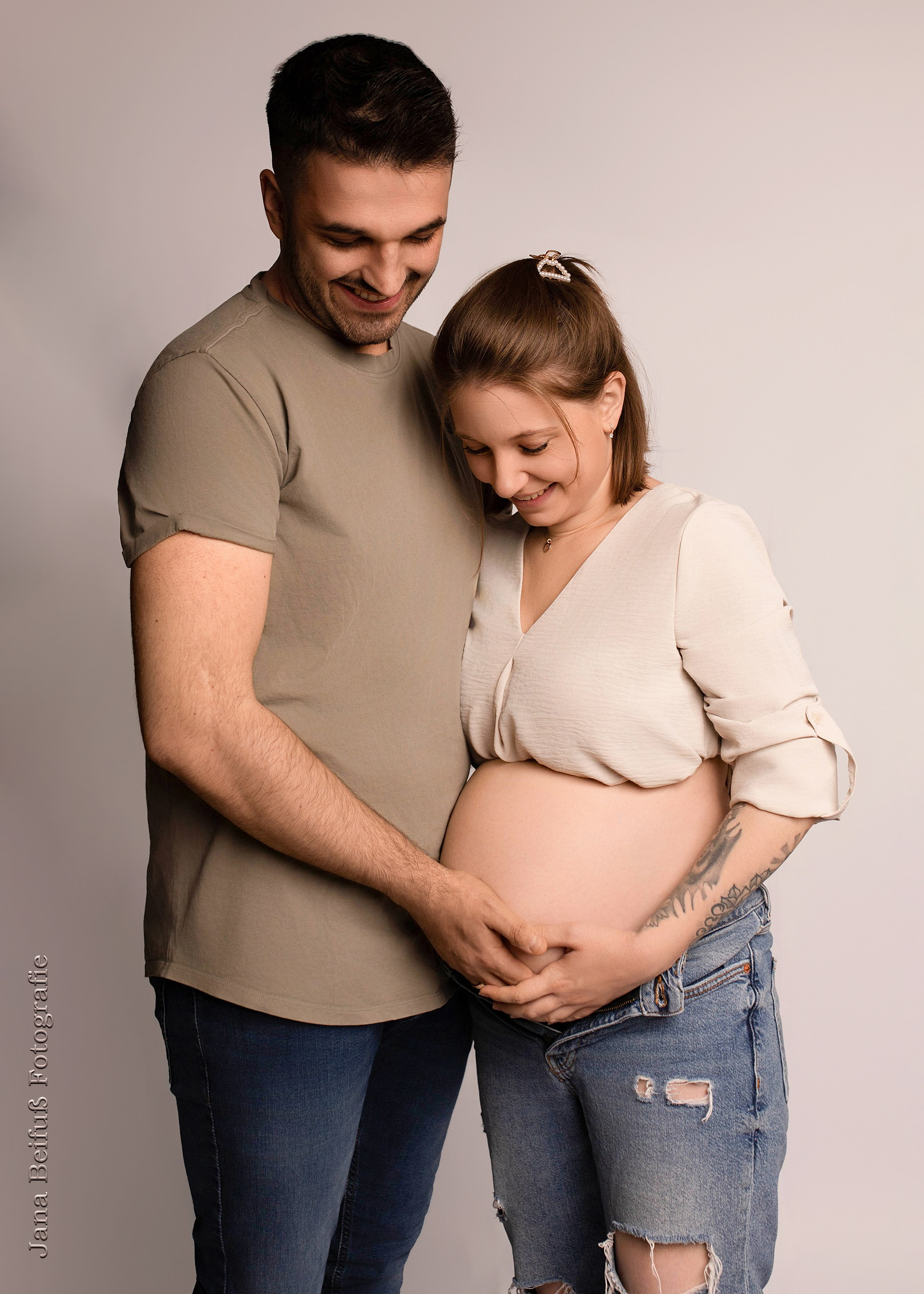 werdende Eltern in Jeans und schauen auf den Babybauch - Schwangerschaftsfotograf Ulm bei Neu-Ulm