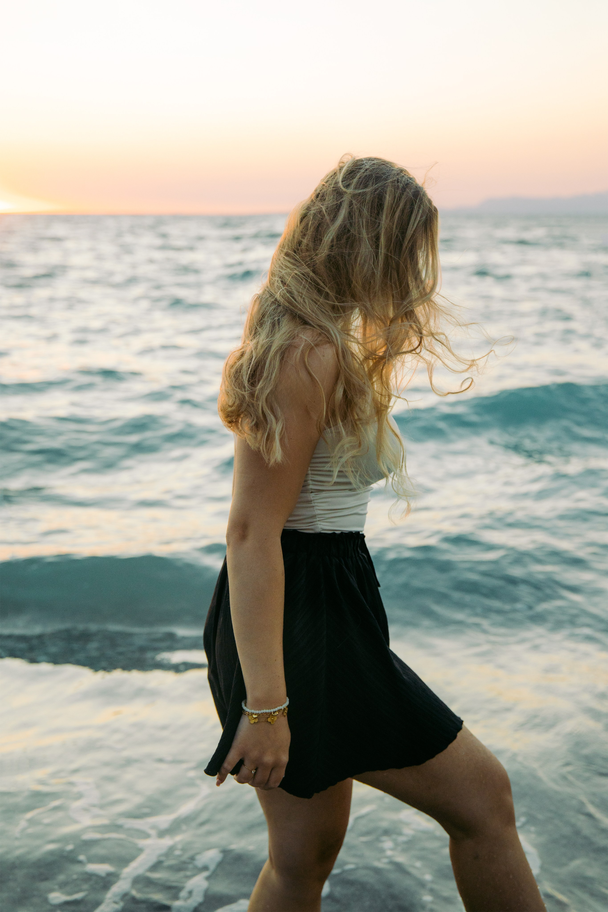 "Glücklicher Moment am Meer: Die Braut geht im seichten Wasser von Kato Petres spazieren. Das Spiel aus Schaumkronen, dunklen Kieselsteinen und dem leuchtenden Türkis des Meeres umrahmt diesen friedlichen Moment nach dem Antrag."