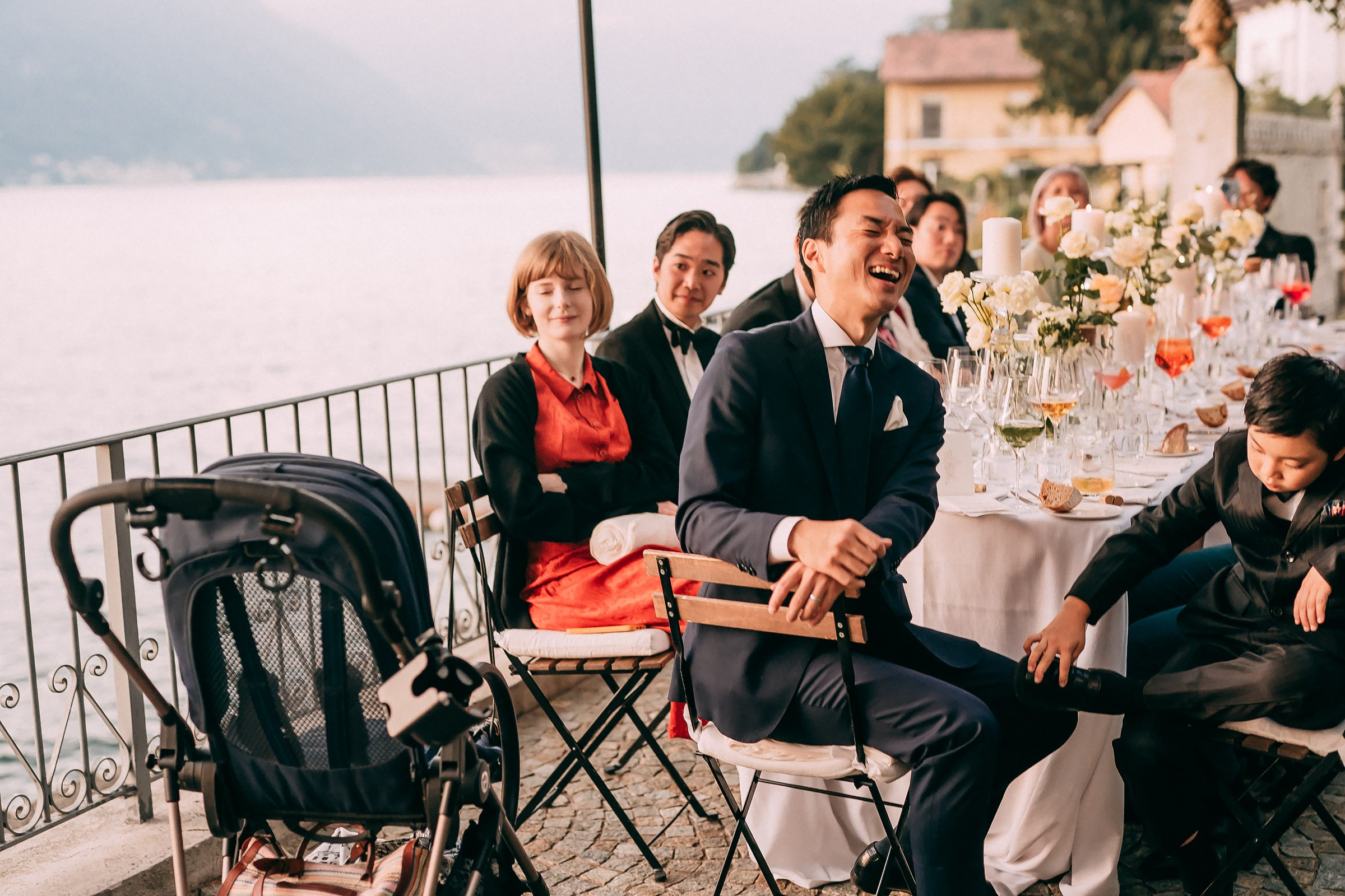 Laughing guest at a lakeside dinner table, surrounded by family and friends, enjoying a festive atmosphere.