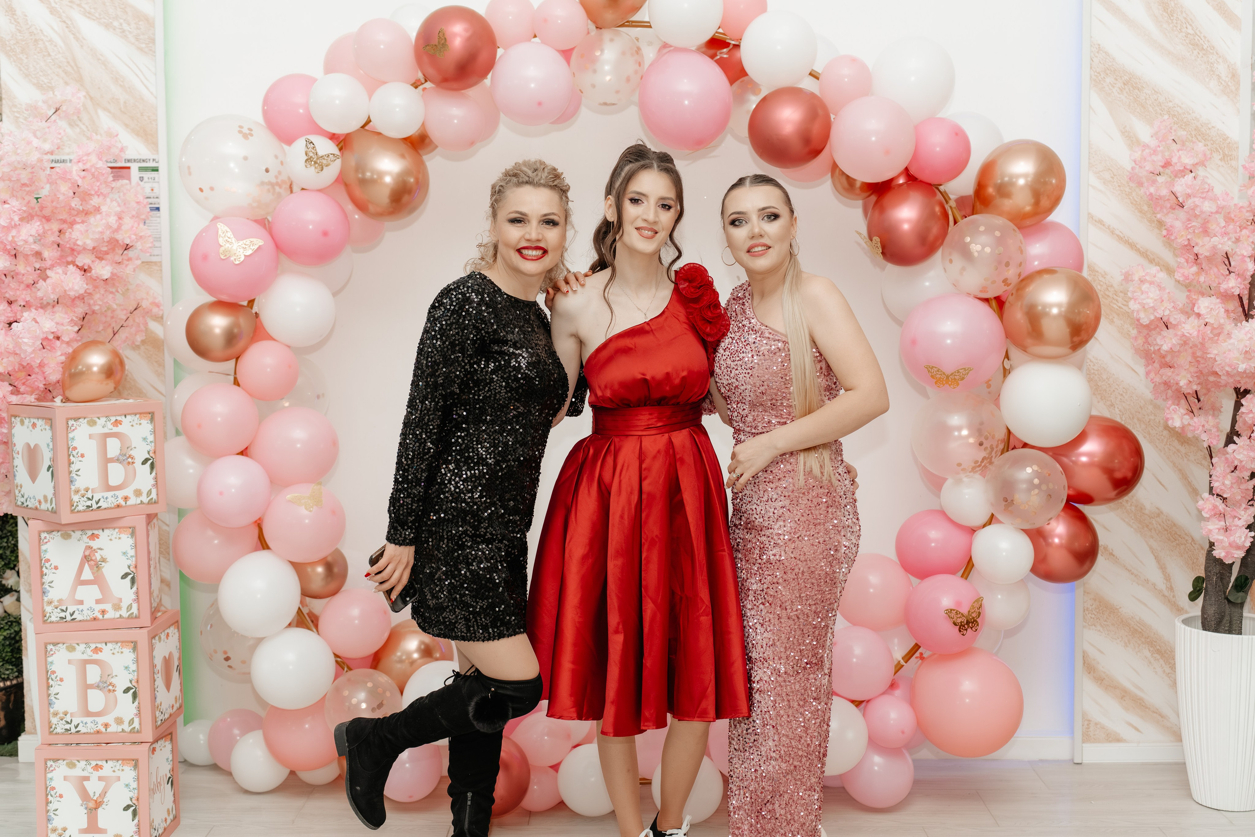 Maria, mama Evelinei Maria, înconjurată de prietenele ei apropiate, toate zâmbind larg și sărbătorind împreună la petrecerea de botez din Restaurantul Silmat, Bălăbănești, Galați. Atmosferă de pură bucurie feminină.