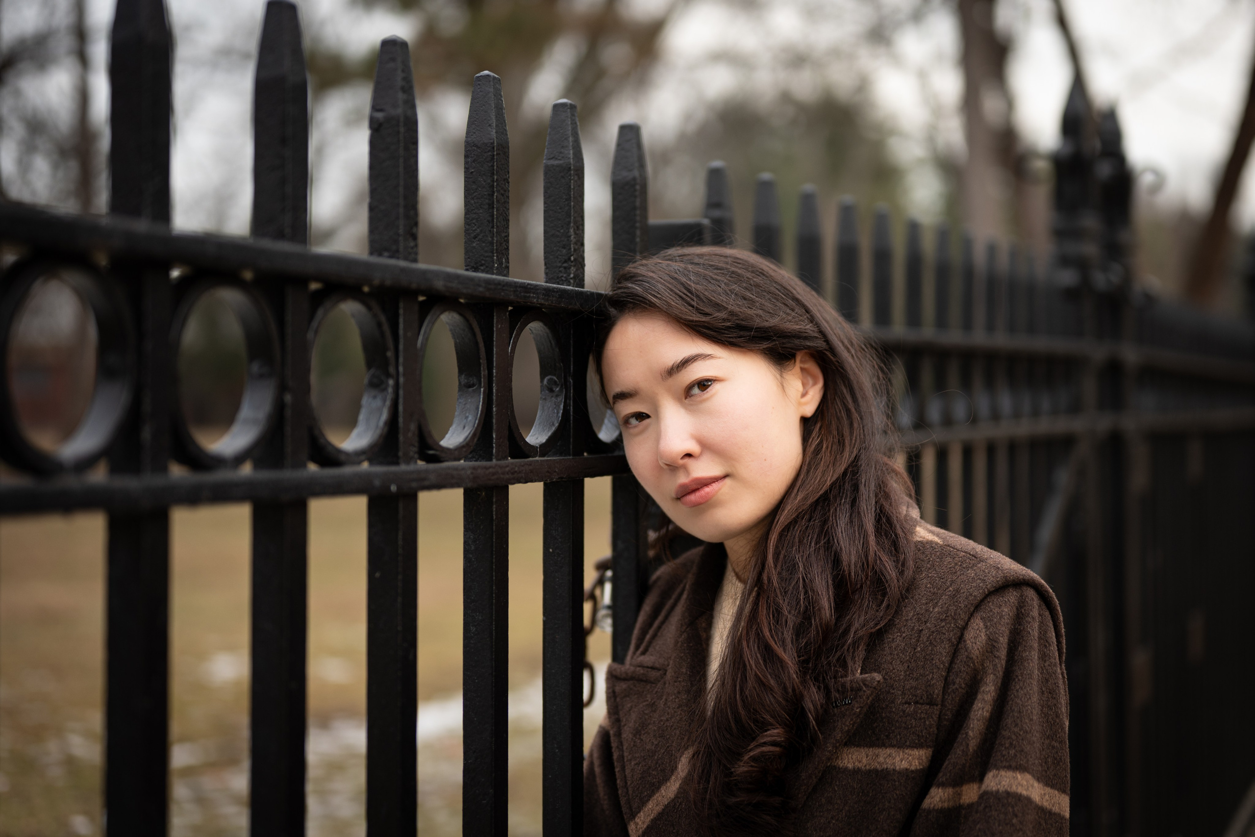 Woman leaning near a black iron fence in Van Cortlandt Park, Bronx, New York, natural light portrait photography.