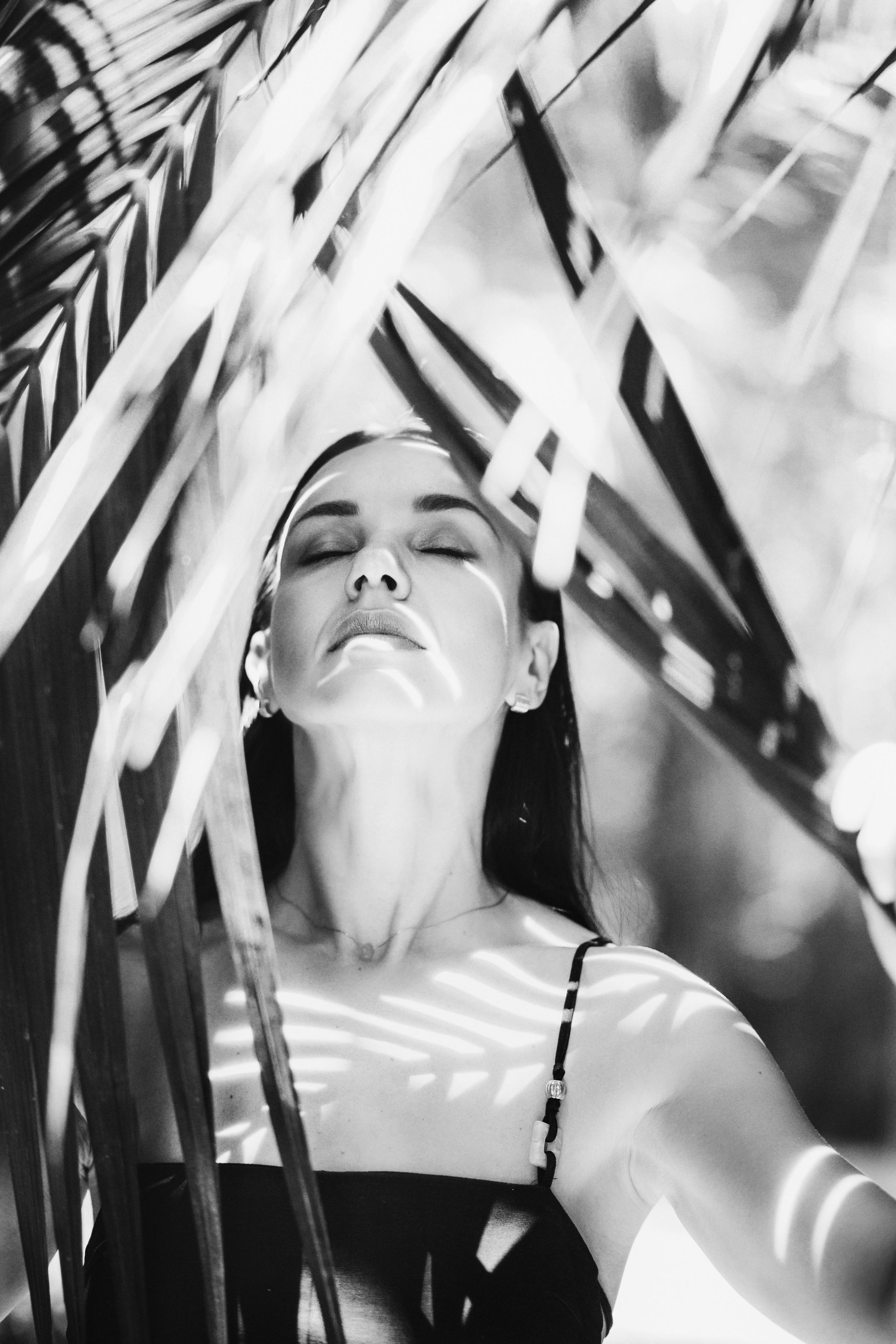Художественный черно-белый портрет спокойной женщины с закрытыми глазами, окруженной пальмовыми листьями в Аликанте, Испания — выразительная портретная фотография, подчеркивающая эмоции, контраст и натуральные текстуры, идеально подходящая для уникальных портретных фотосессий в Аликанте и Испании.