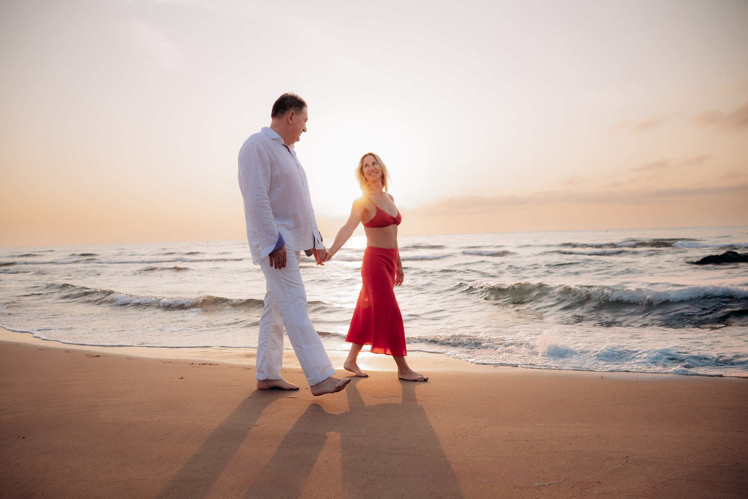 Romantic couple walking hand in hand along the shore at sunrise in Alicante, Spain — candid and joyful love story photography capturing golden light, authentic connection, and the serene Mediterranean beach, perfect for couple photoshoots in Alicante and Spain.
