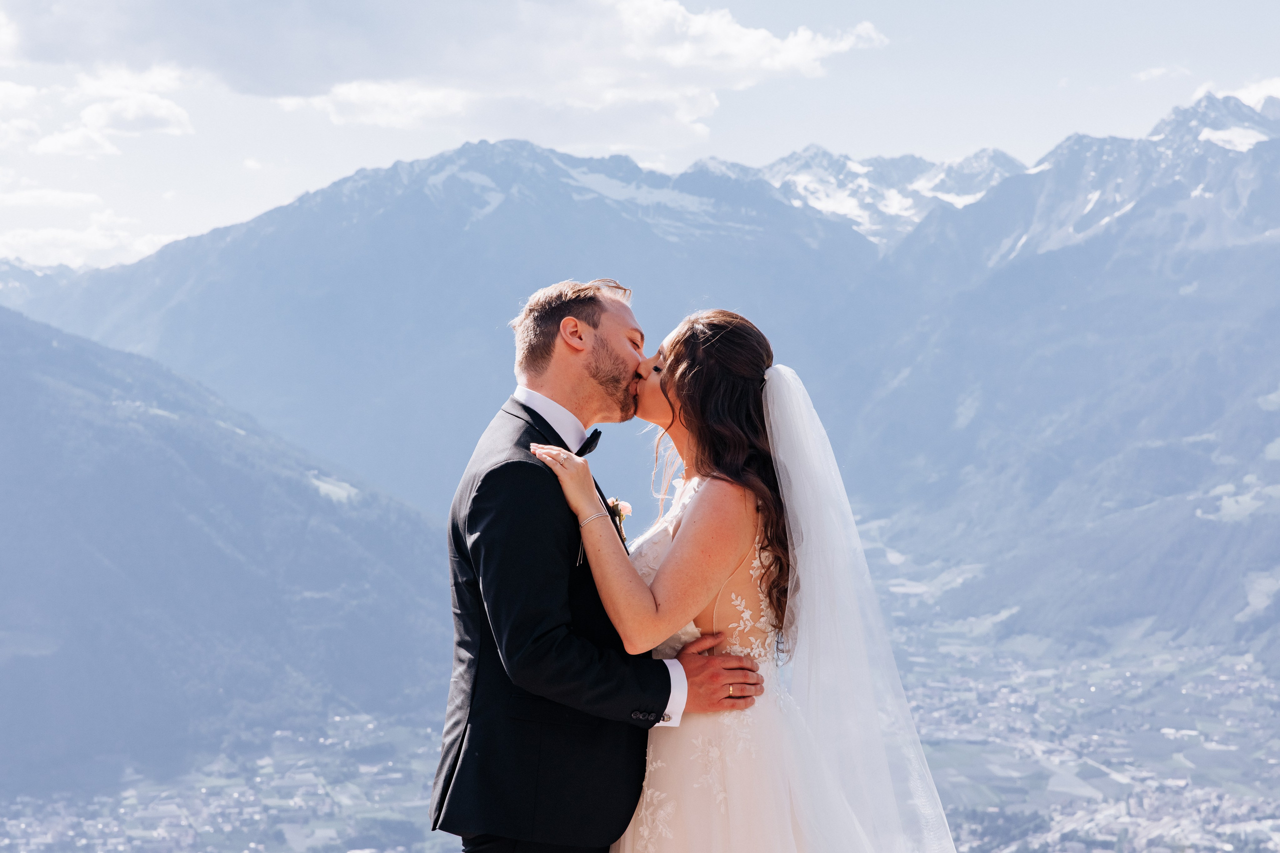 Die Braut und der Bräutigam küssen sich zärtlich vor dem beeindruckenden Bergpanorama in Südtirol.