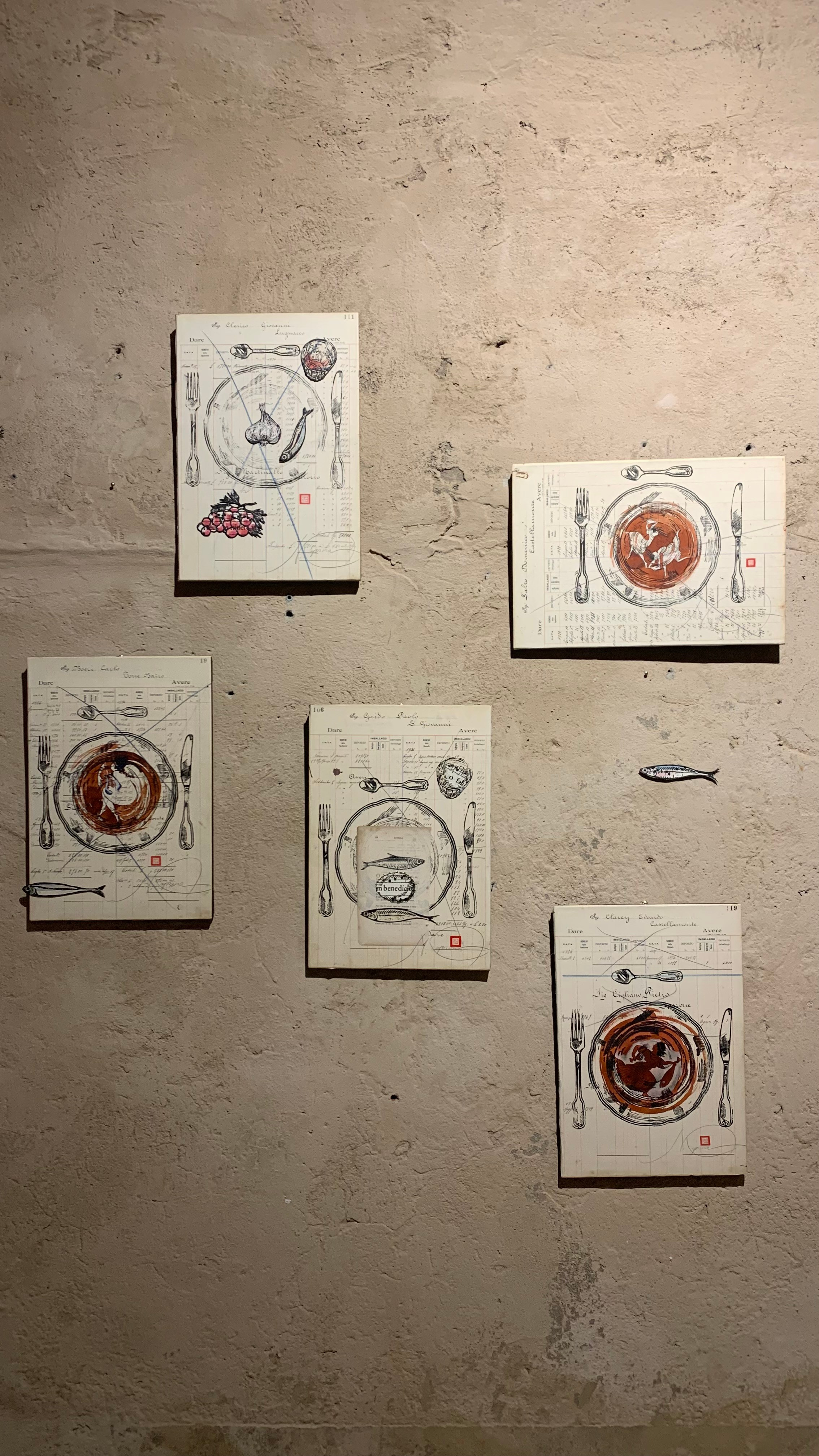 La serie Panem Quotidianum di Nadia Kuprina intreccia memoria italiana e suggestioni elleniche. Su pagine di un registro piemontese del primo Novecento, l’artista stampa a mano piatti e posate in linoleografia. Il piatto, dipinto in seppia, si ispira ai motivi decorativi delle antiche ceramiche greche, evocando figure e narrazioni circolari. Come nei vasi ellenici, il piatto diventa superficie narrativa: non solo oggetto d’uso, ma spazio simbolico dove il gesto del nutrirsi si trasforma in storia e rito.