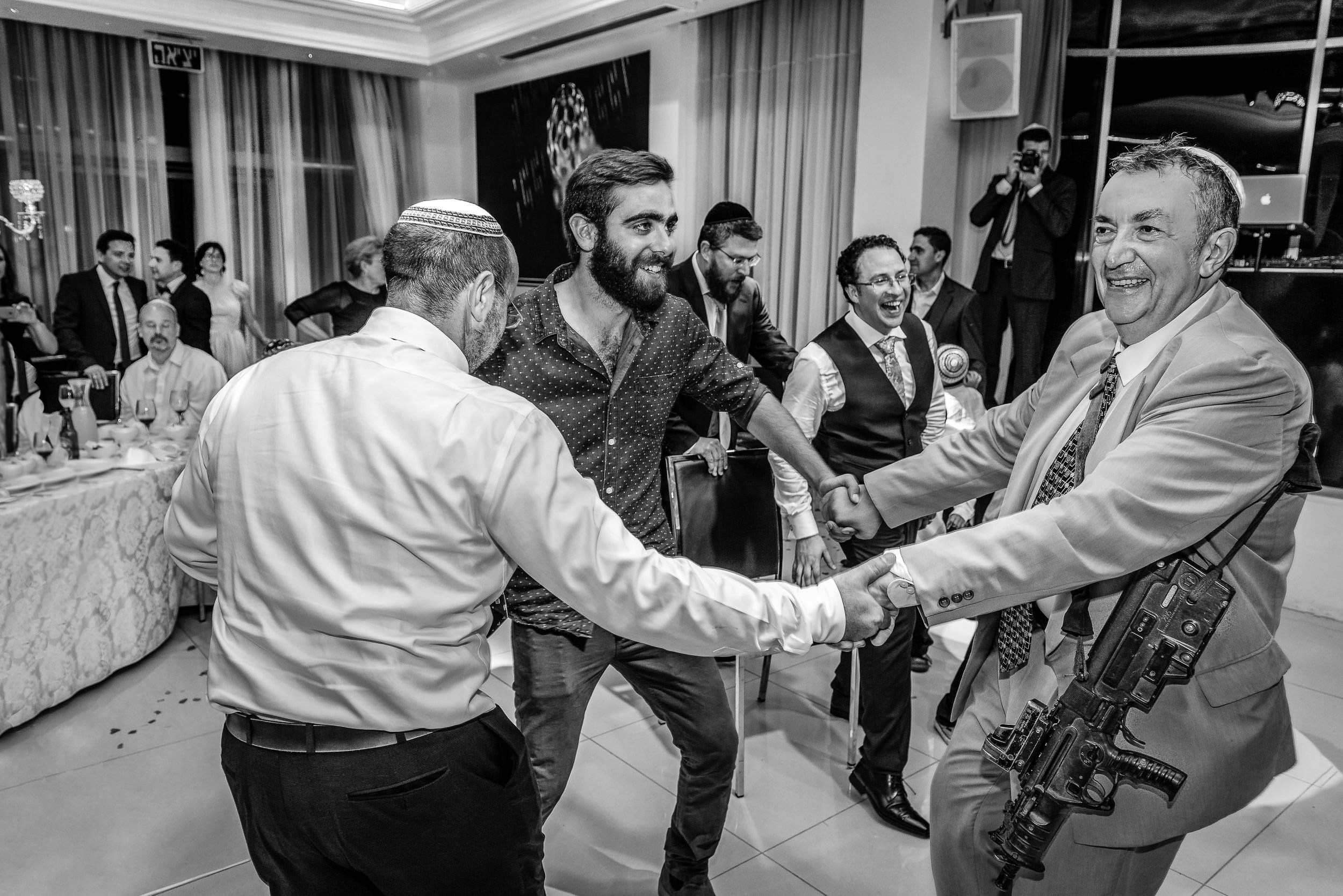Male wedding guests in kippahs dancing together during Simone and Michael's reception at the Leonardo Hotel in Haifa, Israel