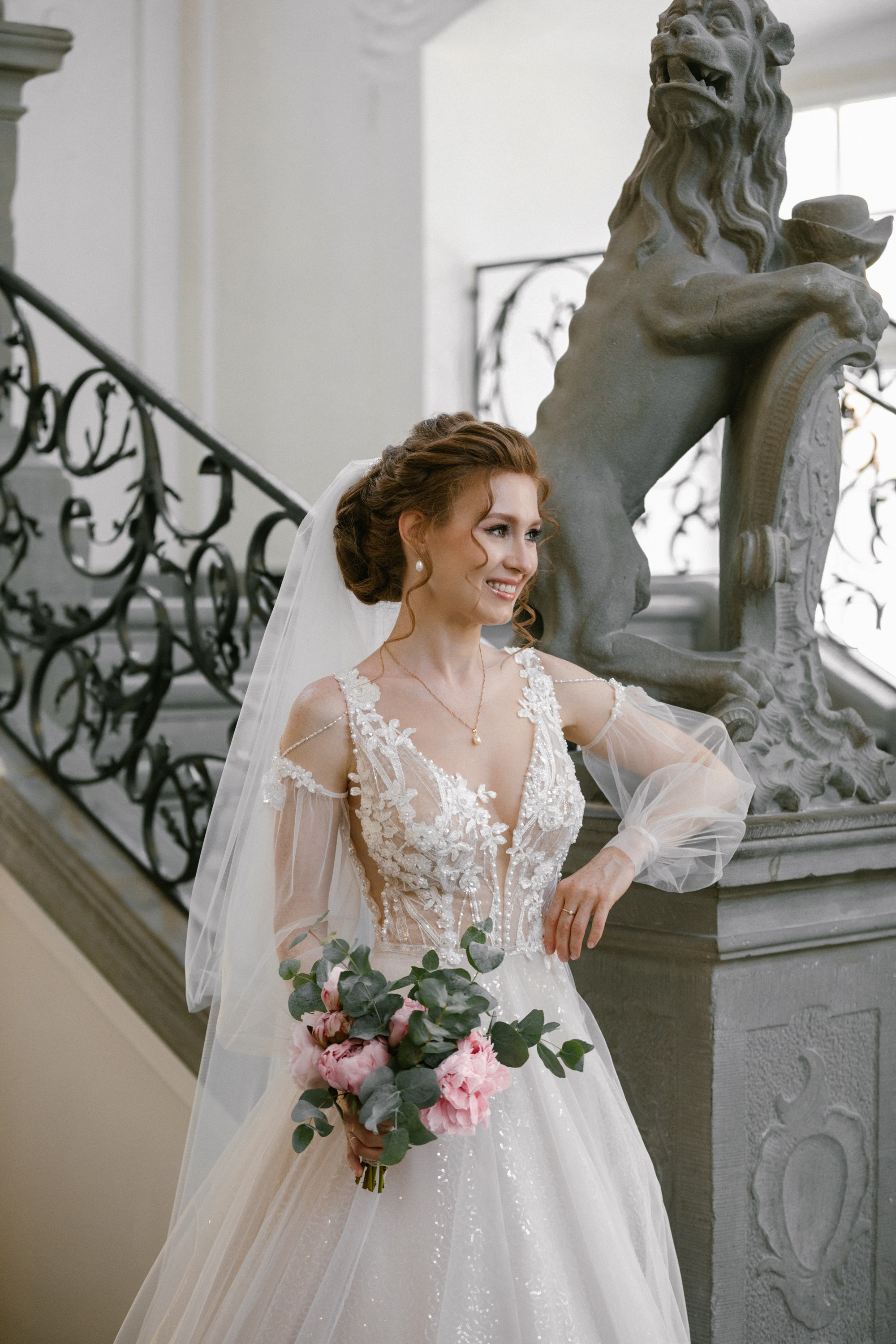 Bride holding bouquet, posing near statue at elegant German castle interior