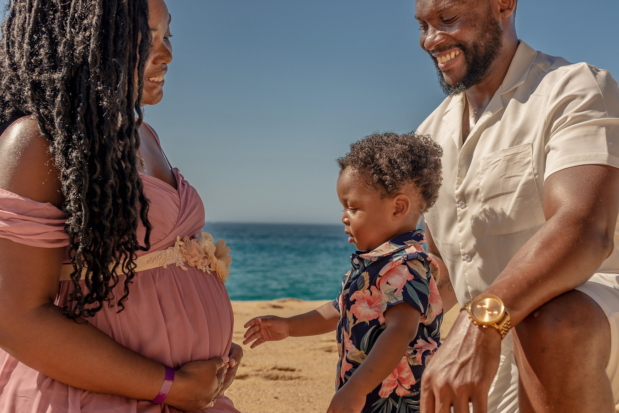 Family maternity photoshoot in Los Cabos – expecting couple with their first child embracing the mother’s baby bump, beach and ocean backdrop, destination family photographer in Cabo San Lucas