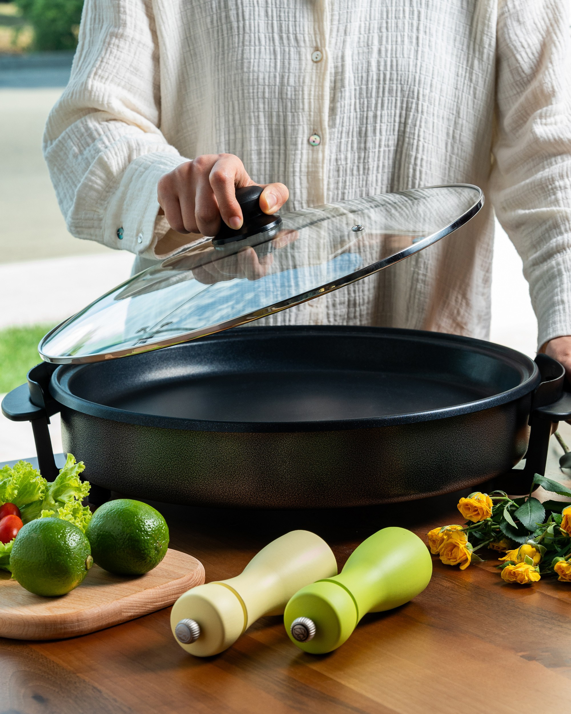 Taxta masanın üzərində əhəng, salat və duz-istiot çalkalayıcıları olan böyük elektrik qazanın şüşə qapağını tutan şəxs.