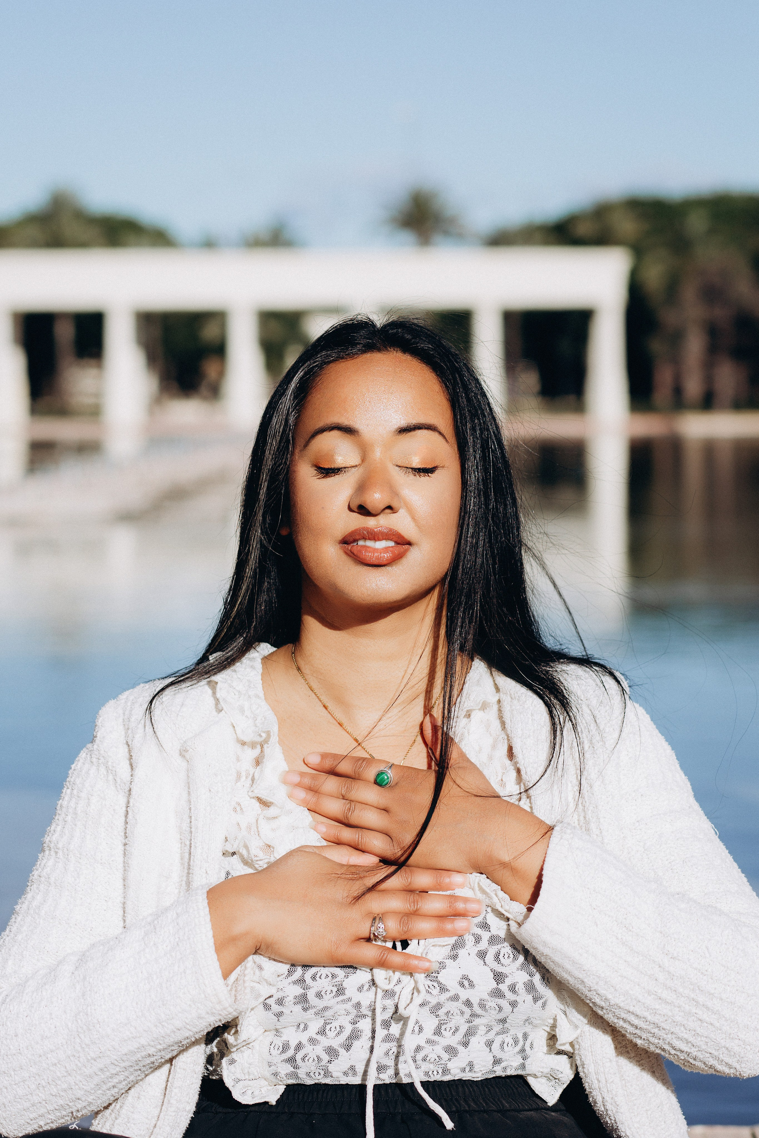 Женская портретная фотосессия в Валенсии, Испания: женщина с закрытыми глазами держит руки на груди у отражающего бассейна с современной архитектурой, создавая спокойную и эмоциональную атмосферу.