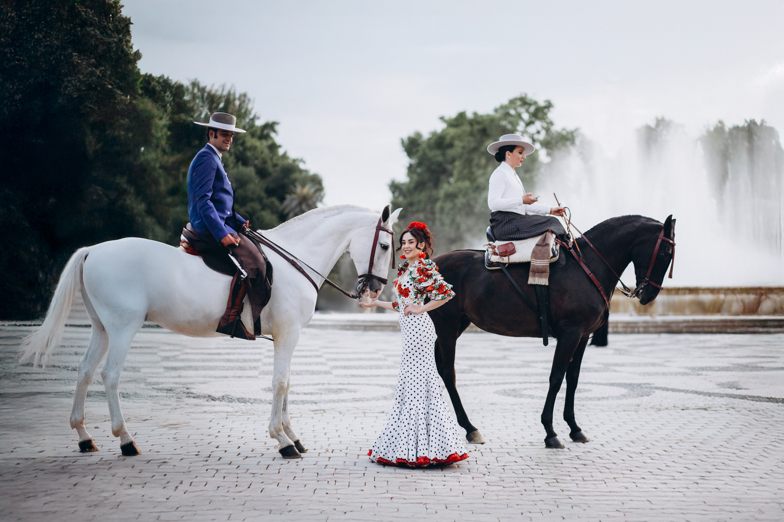 Традиционная испанская портретная фотосессия в Севилье, Испания — женщина в платье фламенко между двумя всадниками в классических андалузских костюмах, идеально подходит для культурных и конных портретных съёмок в Севилье и южной Испании.