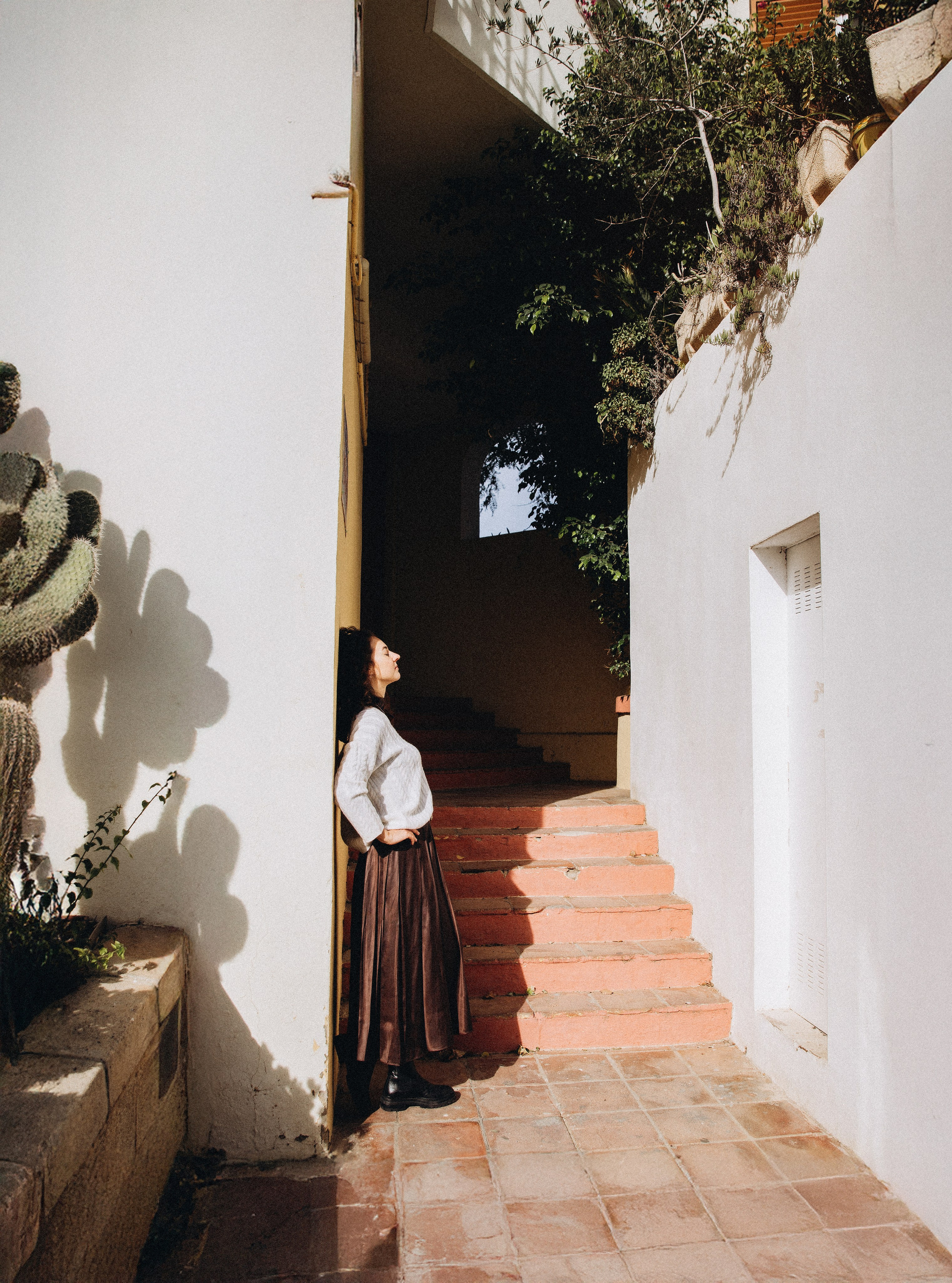 Женская фотосессия в Валенсии, Испания, где женщина стоит в узком историческом переулке с белыми средиземноморскими стенами, тёплым солнечным светом и естественными тенями, создавая поэтичное и художественное настроение — идеально для женской портретной фотографии, лайфстайл-съёмок, fine-art-портретов и профессиональных женских фотосессий в Валенсии и по всей Испании.