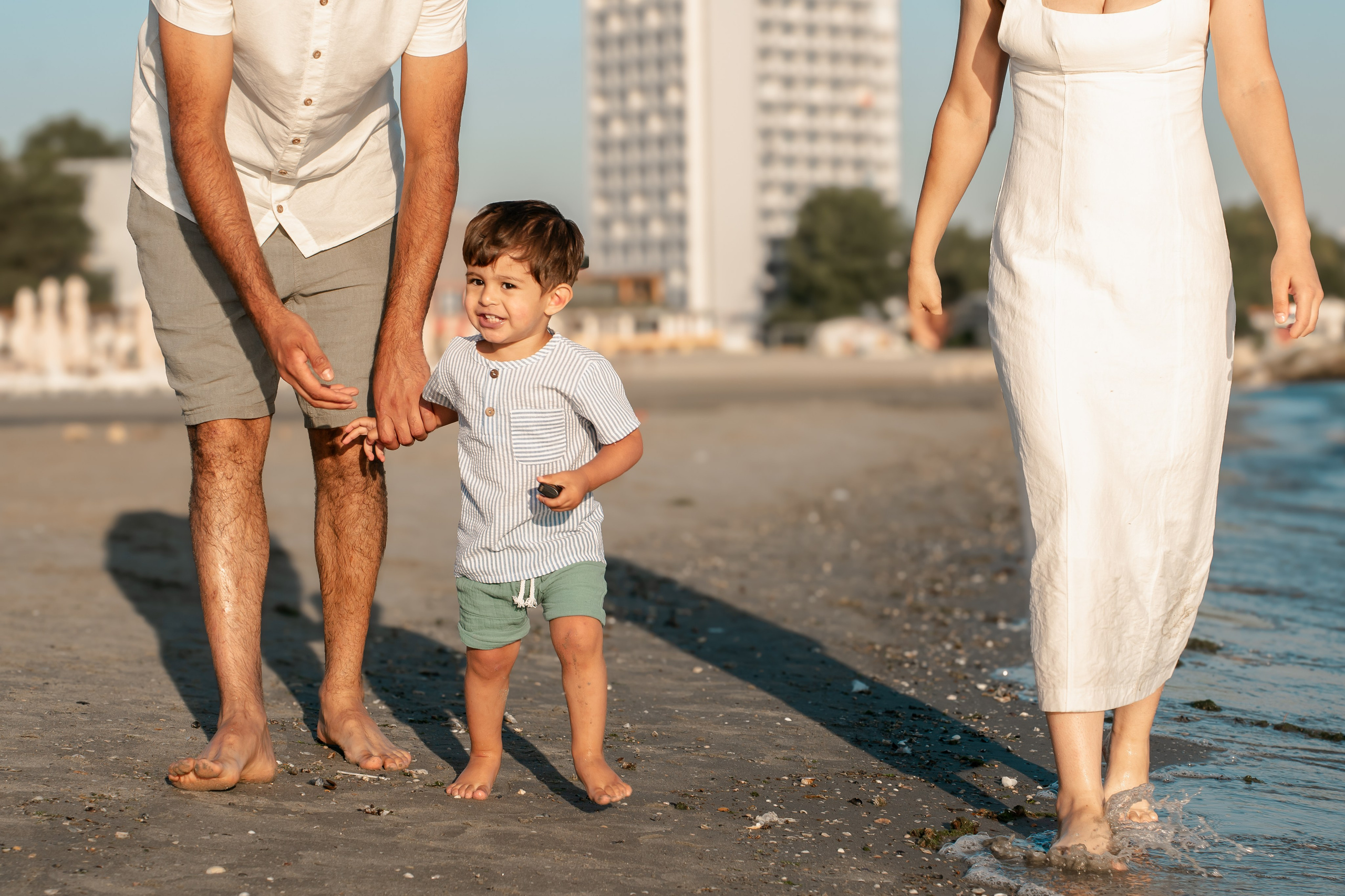 baietel care se plimba de mana cu parintii pe plaja