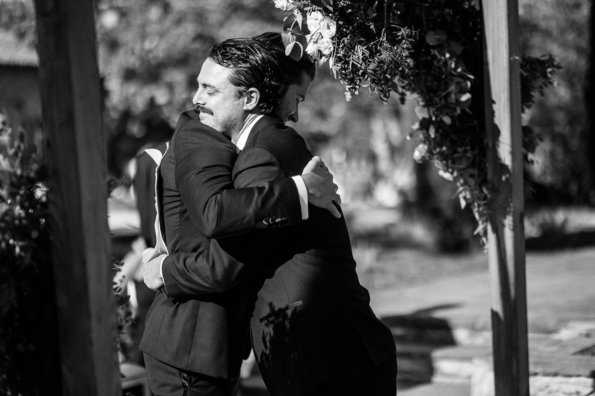 An emotional hug between the groom and the officiant, captured in a candid black-and-white moment during the outdoor ceremony in Provence, France.