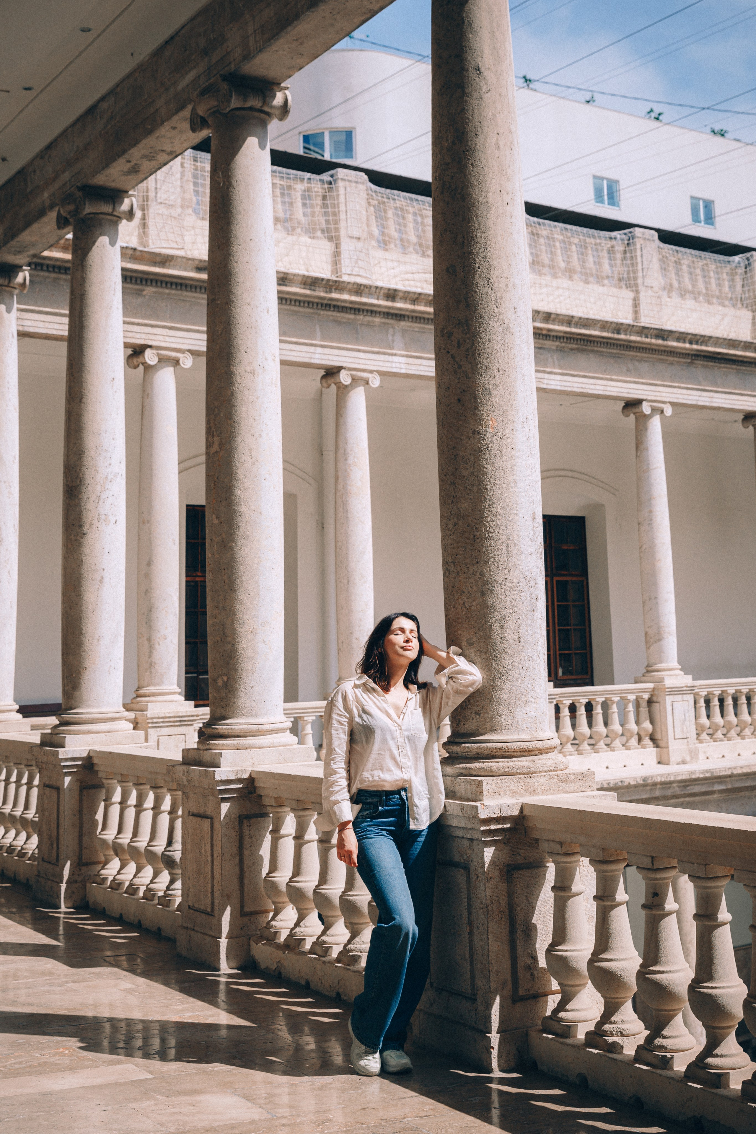 Арт-портретная фотосессия в Мадриде, Испания — стильная женщина позирует в исторической колоннаде, залитой естественным светом, идеально для тех, кто ищет классическую и элегантную портретную фотографию в Мадриде и по всей Испании.