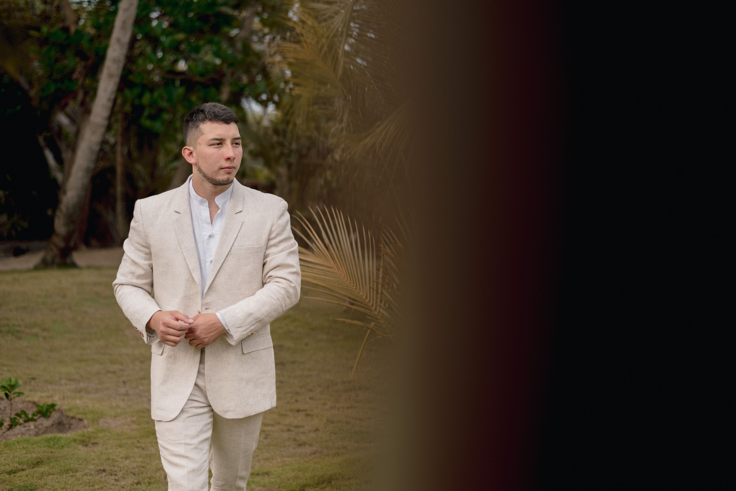 Novio en traje blanco de lino en jardín, retrato elegante de ceremonia matrimonial tropical