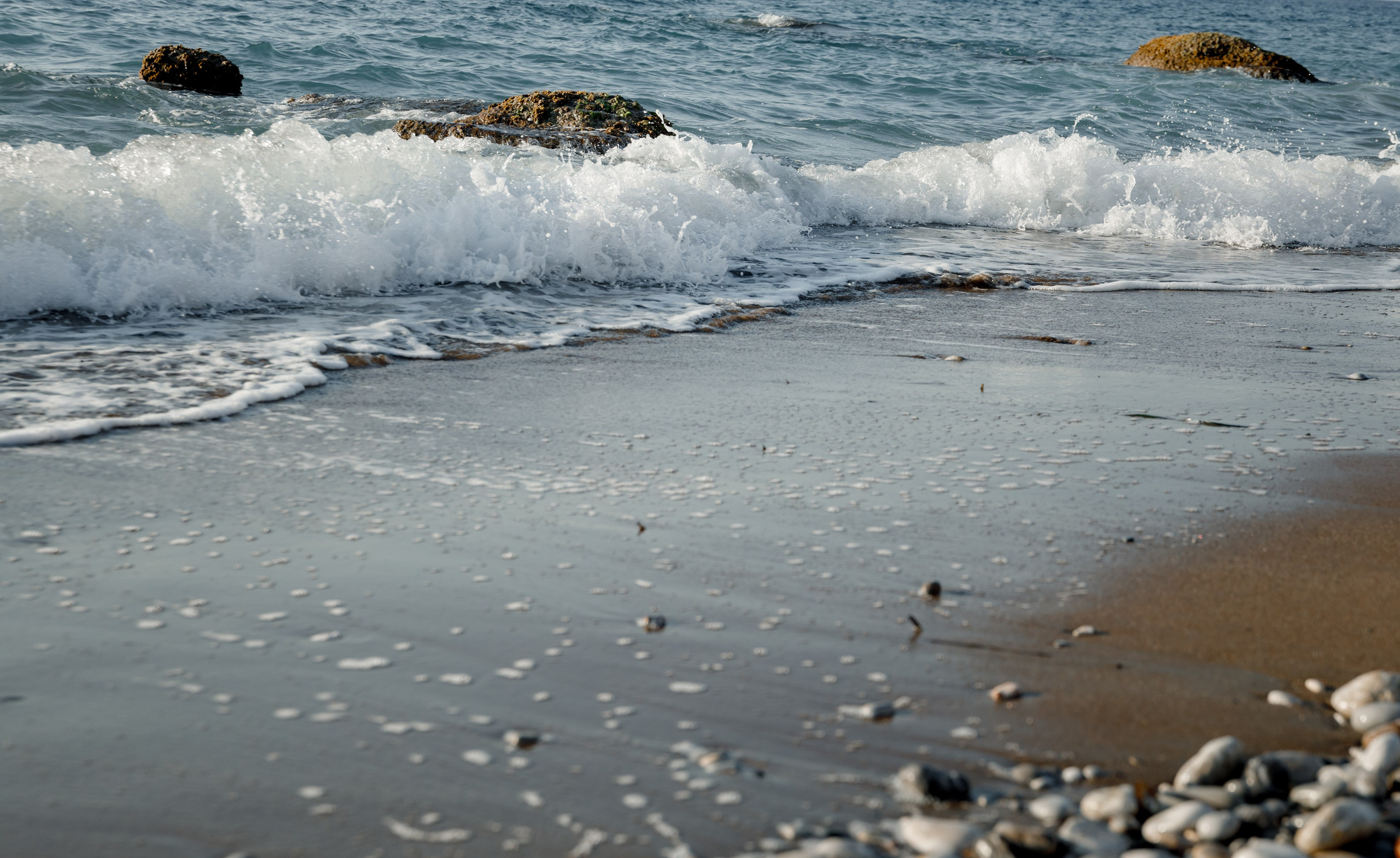 "Blick auf die charakteristischen Kalksteinfelsen am Strand von Kato Petres. Die von Wind und Wasser geformten Höhlungen in den Klippen bieten einen starken Kontrast zum klaren, türkisfarbenen Wasser und dem hellen Kieselstrand."