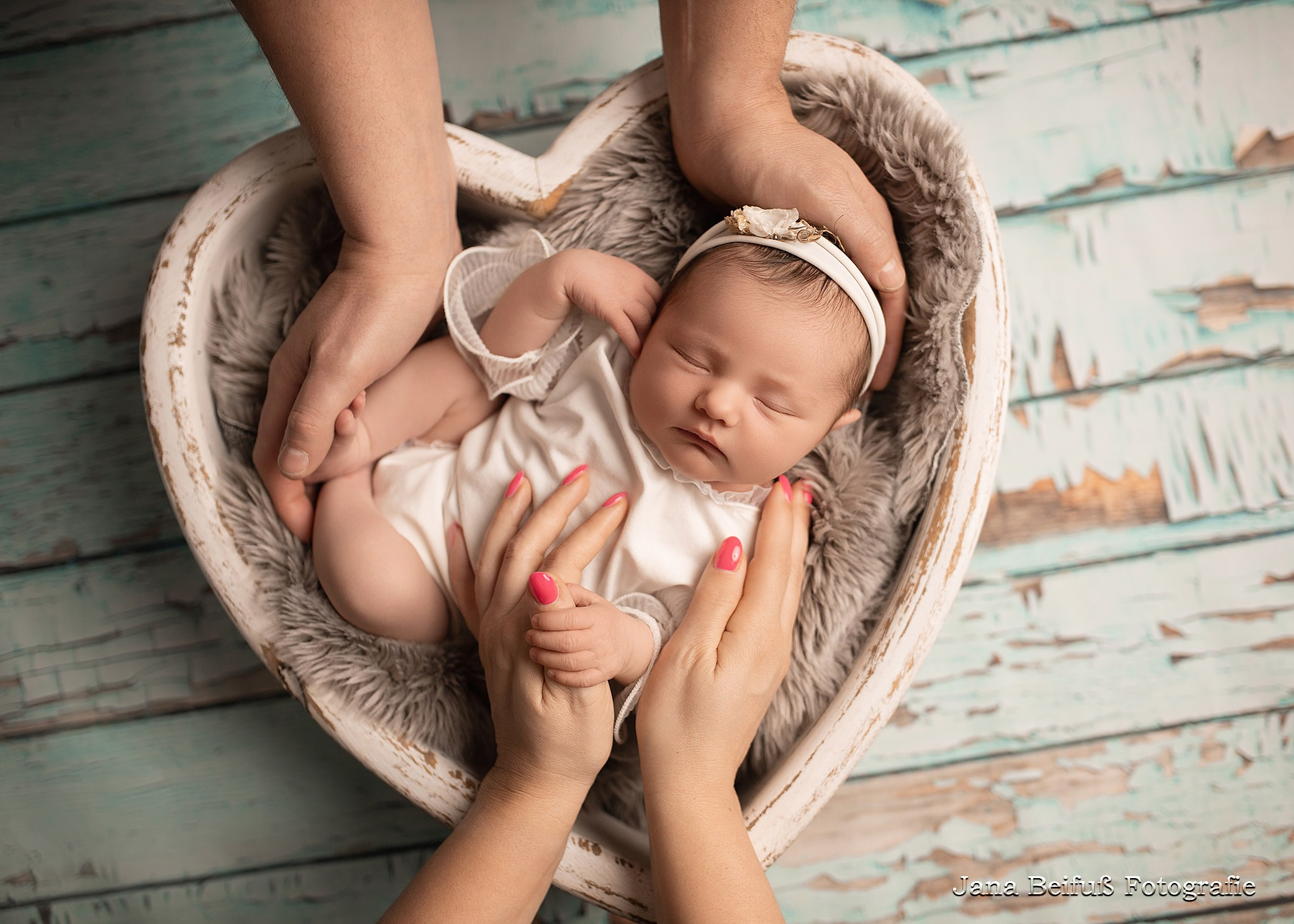Baby schläft in weißem Herz auf Holzboden Eltern halten Baby in den Händen Fotograf Jana Beifuß Nähe Ulm