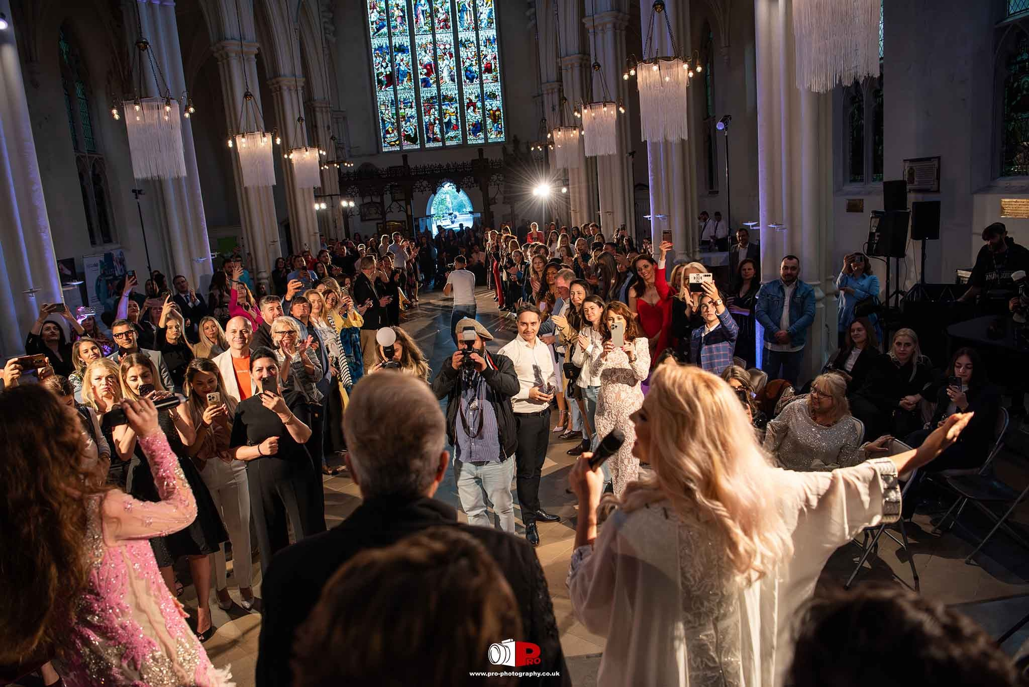 A crowd of enthusiastic attendees captured the runway show with their smartphones inside a grand cathedral.