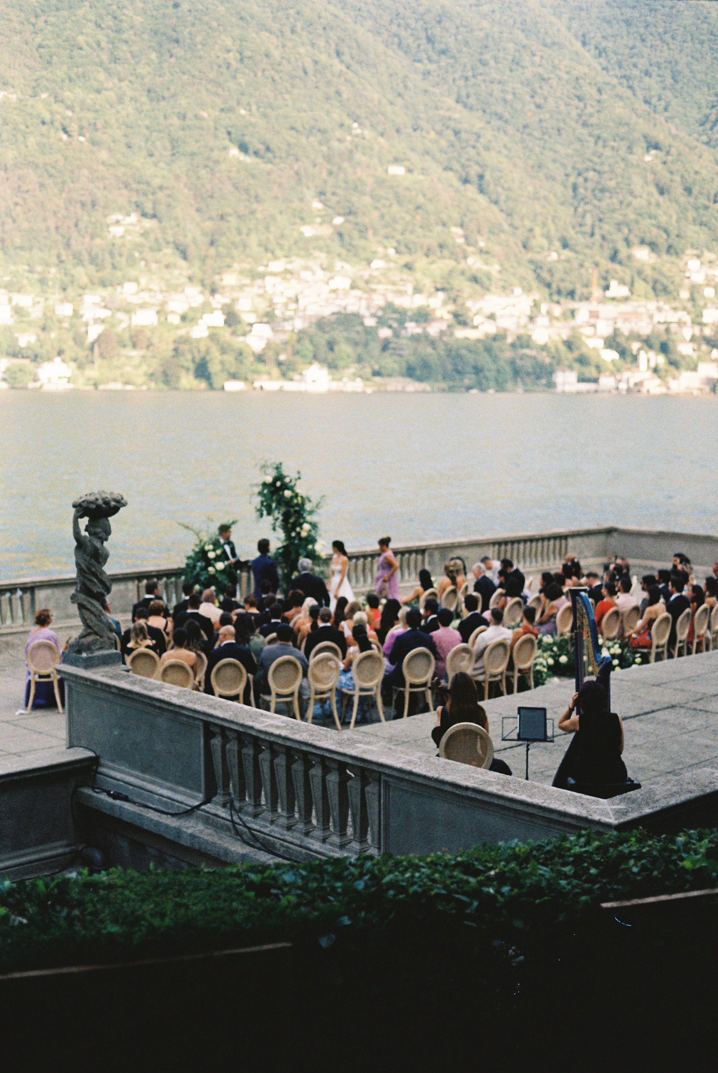 Wedding ceremony by the lake Como with mountain view and guests seated outdoors.