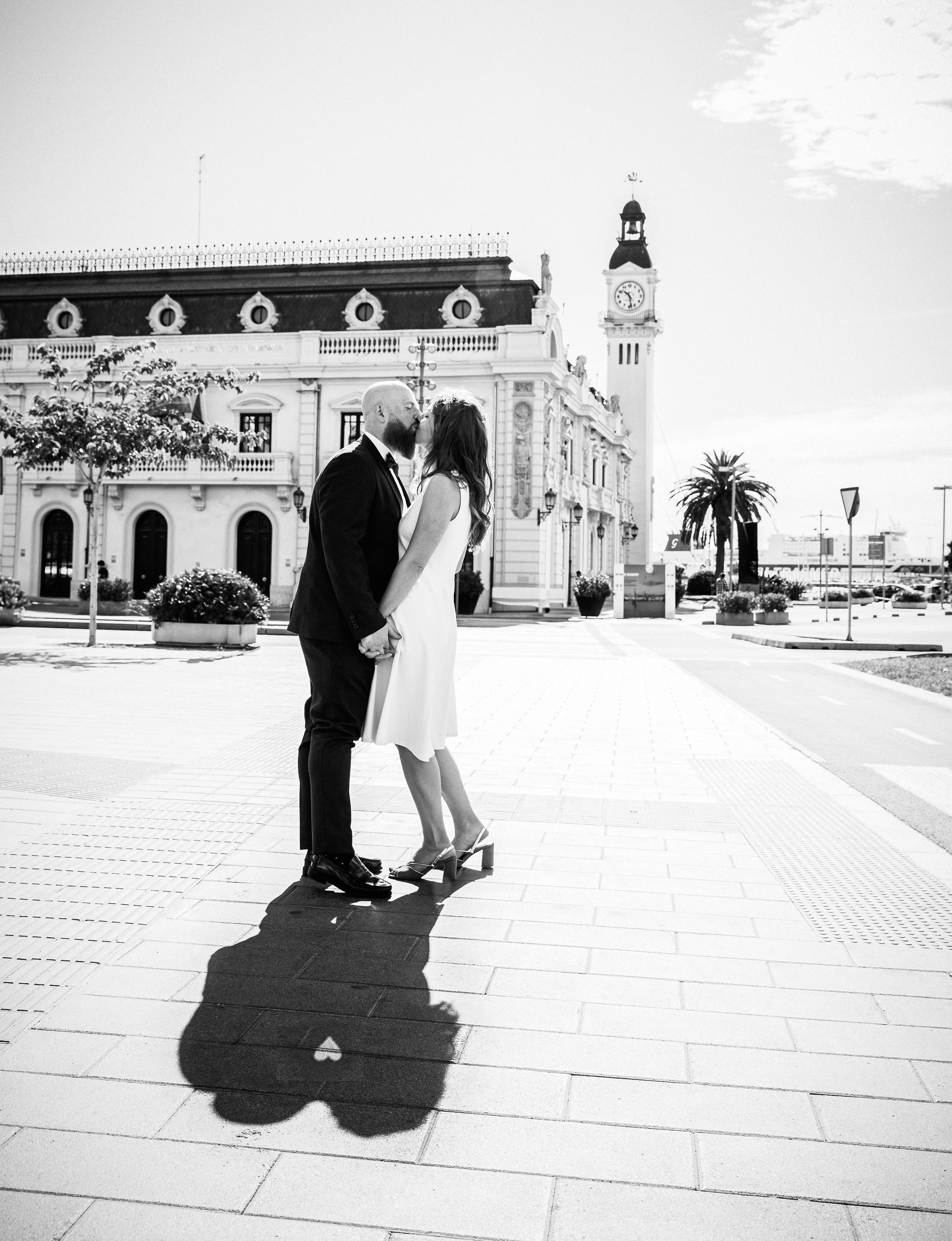 Bride and groom share a kiss in Plaza del Ayuntamiento during their intimate civil wedding in València. The timeless black-and-white wedding portrait highlights the architectural beauty and urban charm of a city hall celebration in Spain.