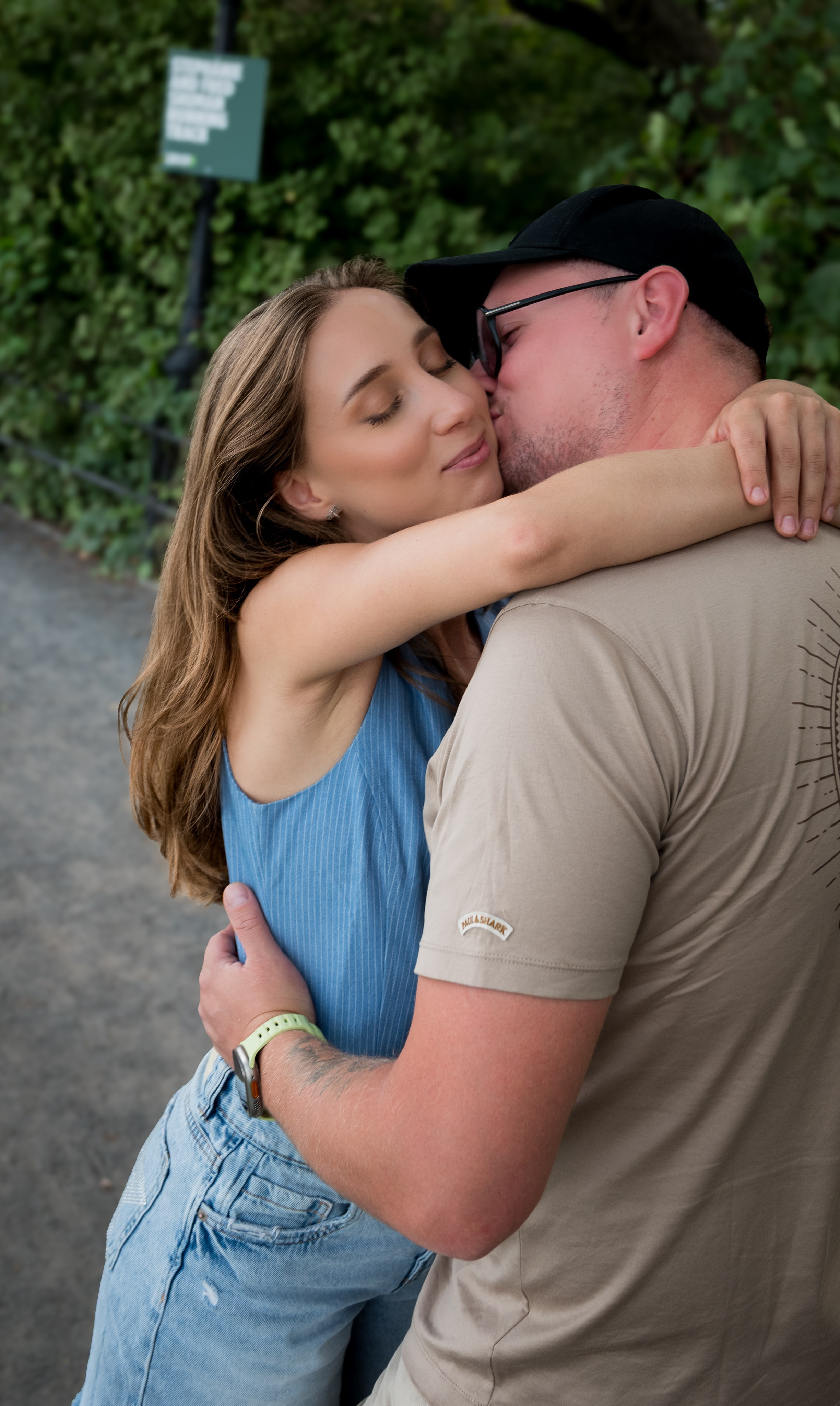 Couple kissing while hugging outdoors, intimate candid portrait in a leafy park, New York City photoshoot.