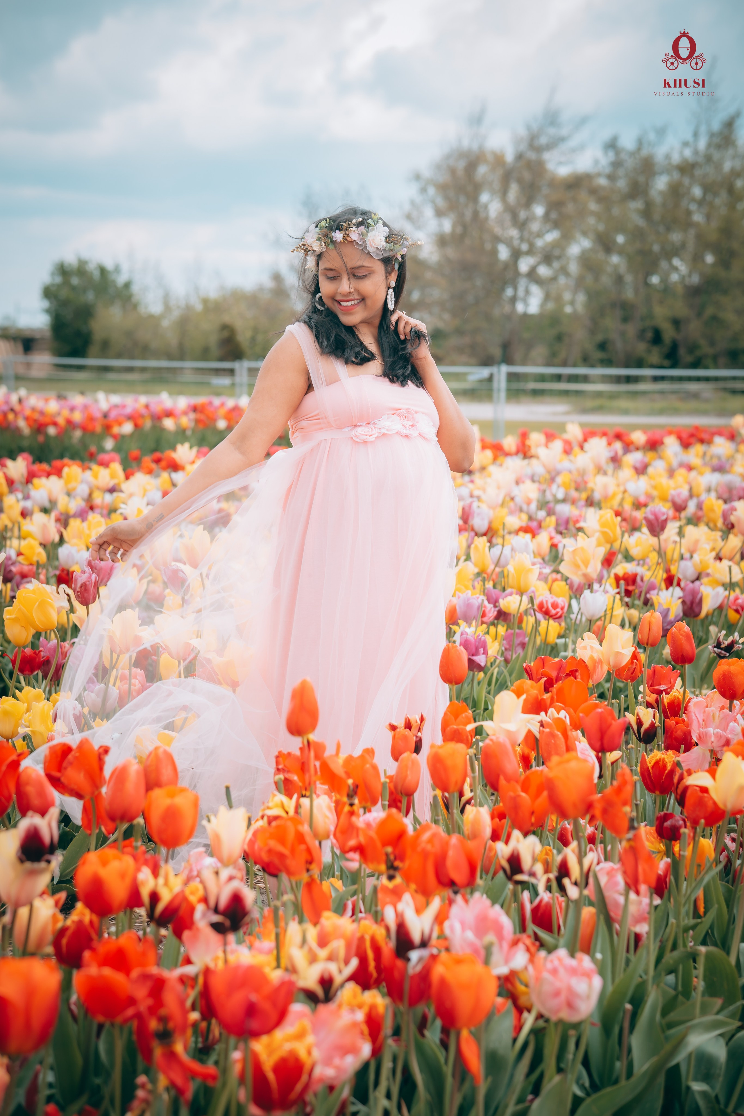 A pregnant woman wearing a pink gown and standing in a tulip fields in netherlands