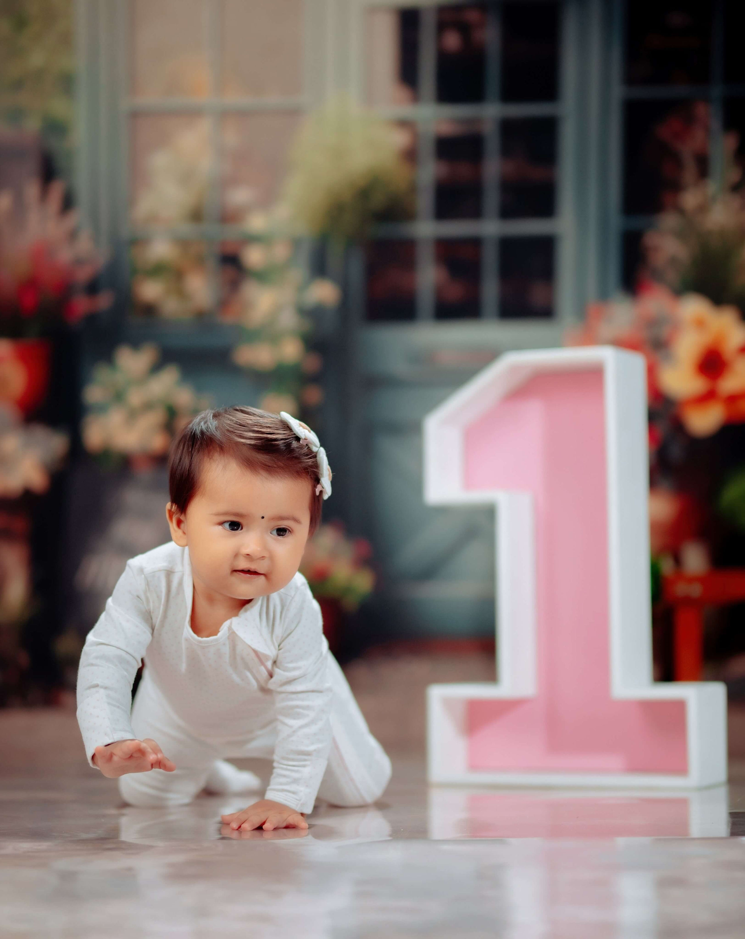 One year old baby girl crawling next to a large pink number one prop photo poudel digital