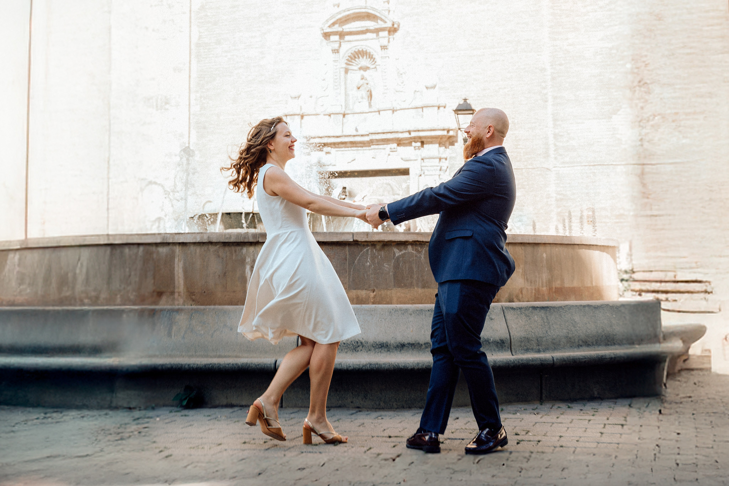 Newlyweds twirl playfully in front of a classic Valencia fountain moments after their civil ceremony. This candid wedding photograph reflects the relaxed, romantic atmosphere of a civil wedding in València, Spain.