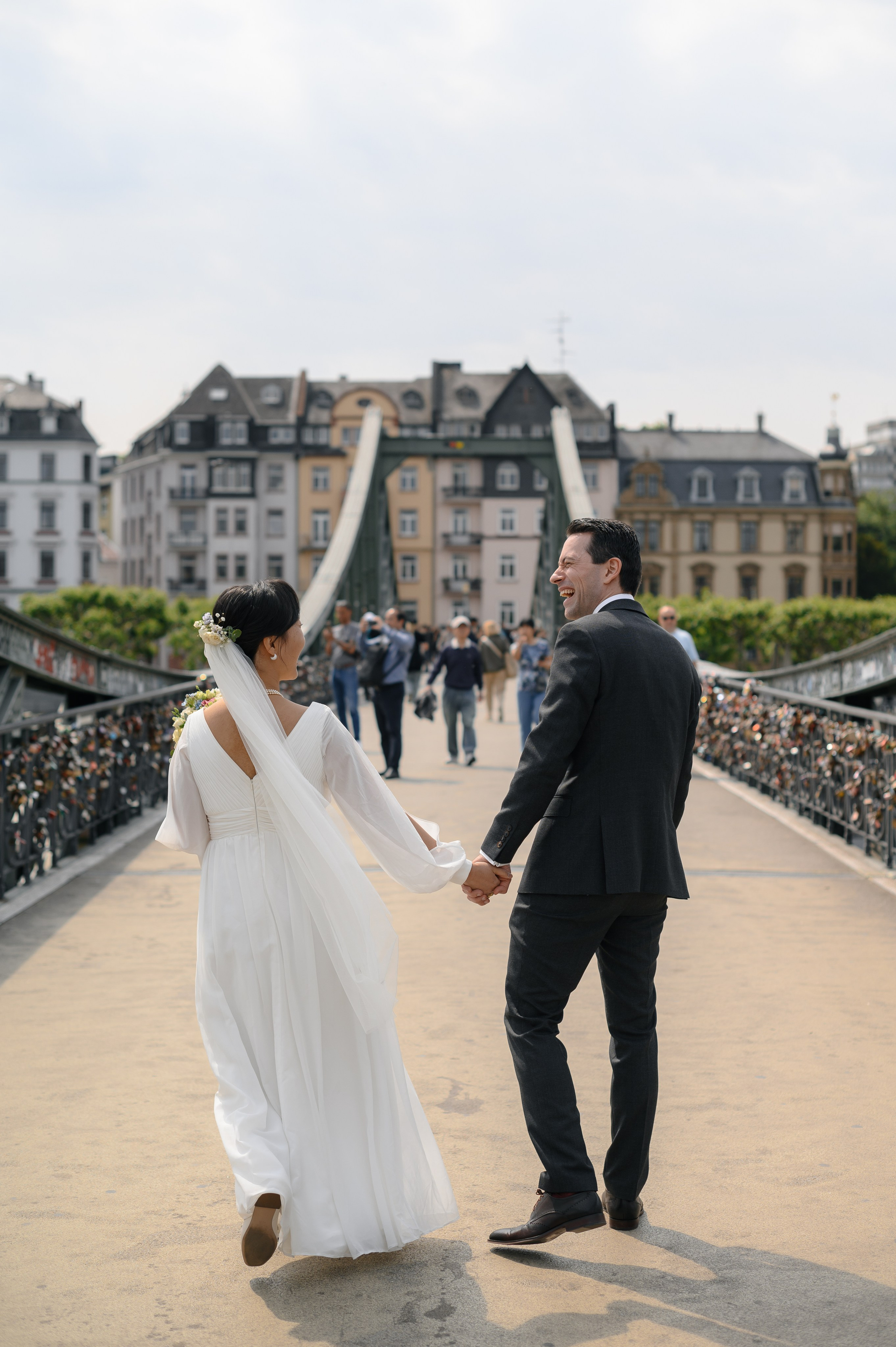 Braut und Bräutigam gehen Hand in Hand über die Brücke am Mainufer
