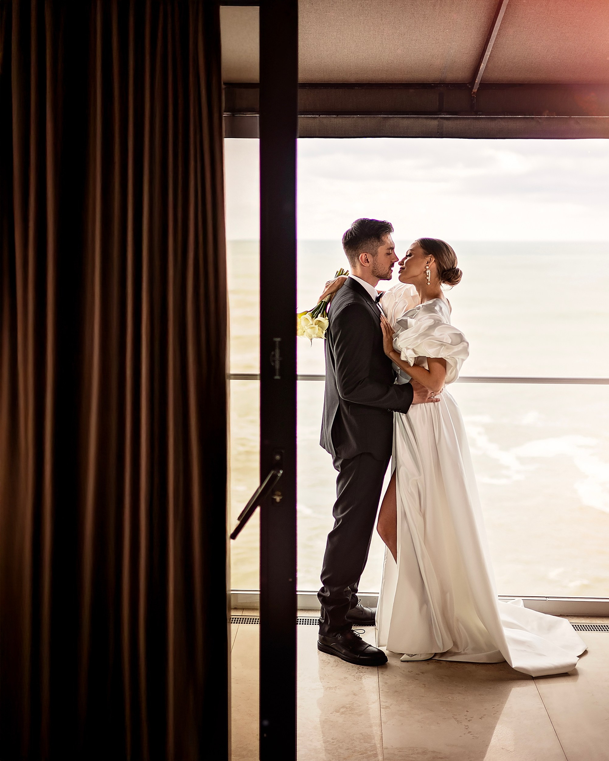 Full-length portrait of a bride and groom embracing on a scenic terrace overlooking the ocean. Creative destination wedding photographer by vdphotoart.