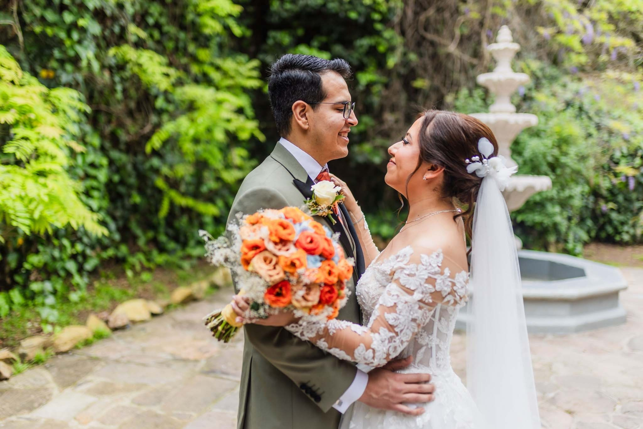 novios abrazados con ramo de flores frente a fuente jardin boda Tijuana Baja California