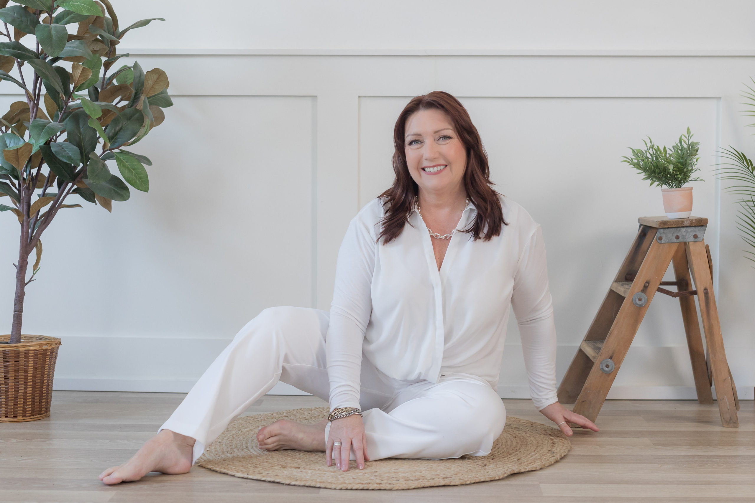 Women wearing all white leisure set sitting on floor in yoga pose 