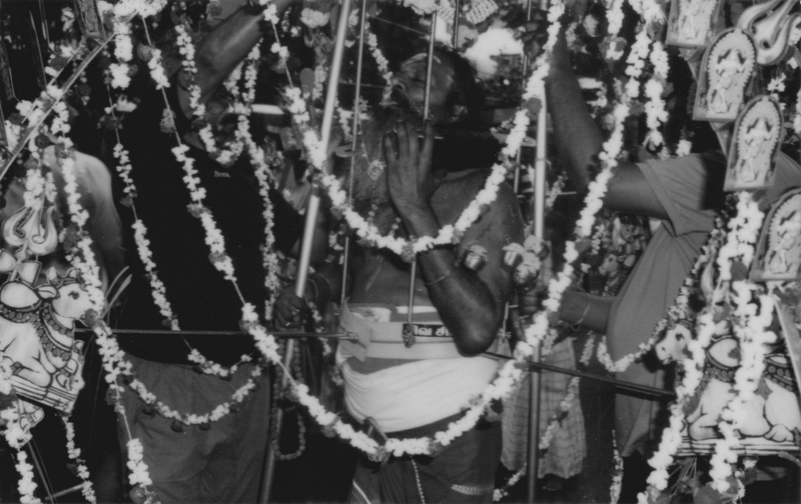 A vibrant black-and-white photograph capturing the intensity of a Thaipusam devotee in the midst of a ritual, surrounded by garlands and ornate decorations in Singapore. The devotee's expression and the intricate ceremonial details convey a powerful story of faith and tradition. This image showcases the photographer’s skill in reportage photography, offering clients dynamic and immersive visual storytelling for cultural, religious, or corporate events.