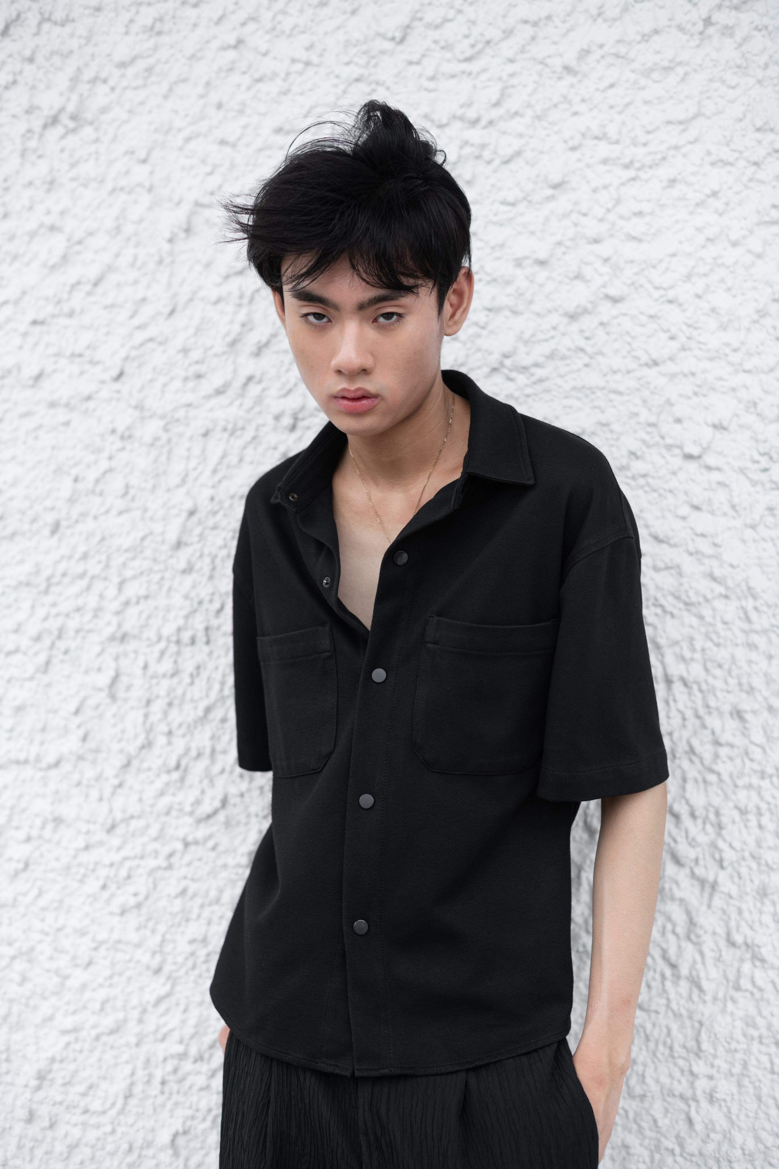 Close-up portrait of a male model with intense gaze, natural lighting, and blurred Singapore urban backdrop, editorial fashion style.