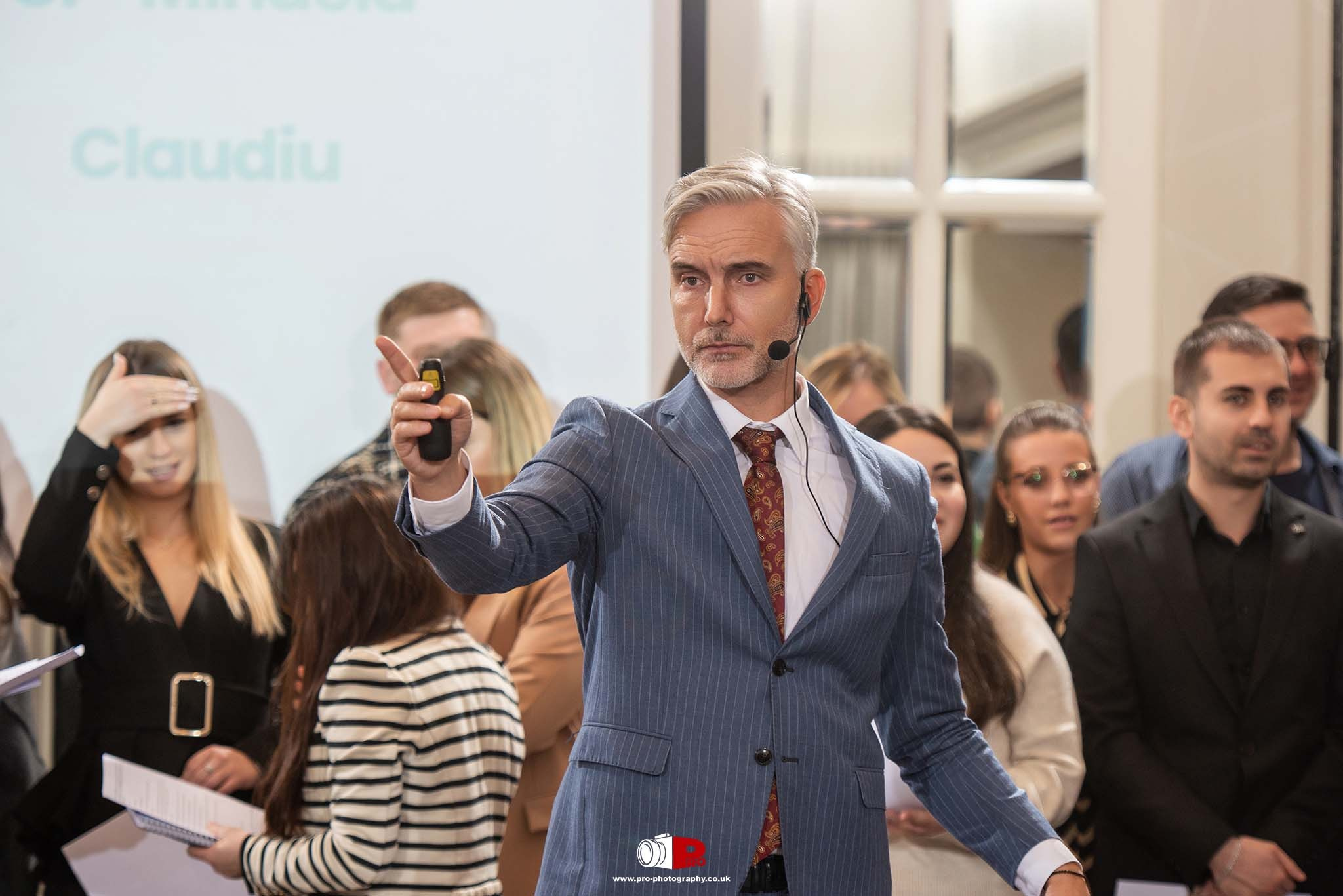 A professional speaker in a blue suit giving a presentation to an audience.